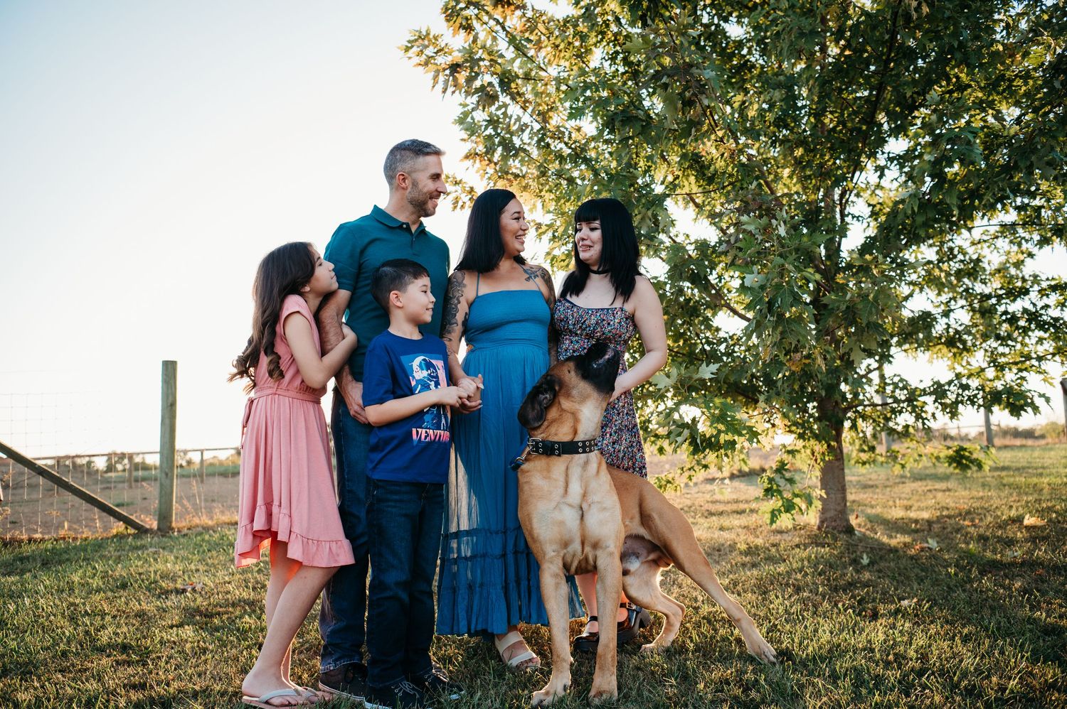 Happy family with two children and a dog gather under a tree during a golden hour outdoor session.