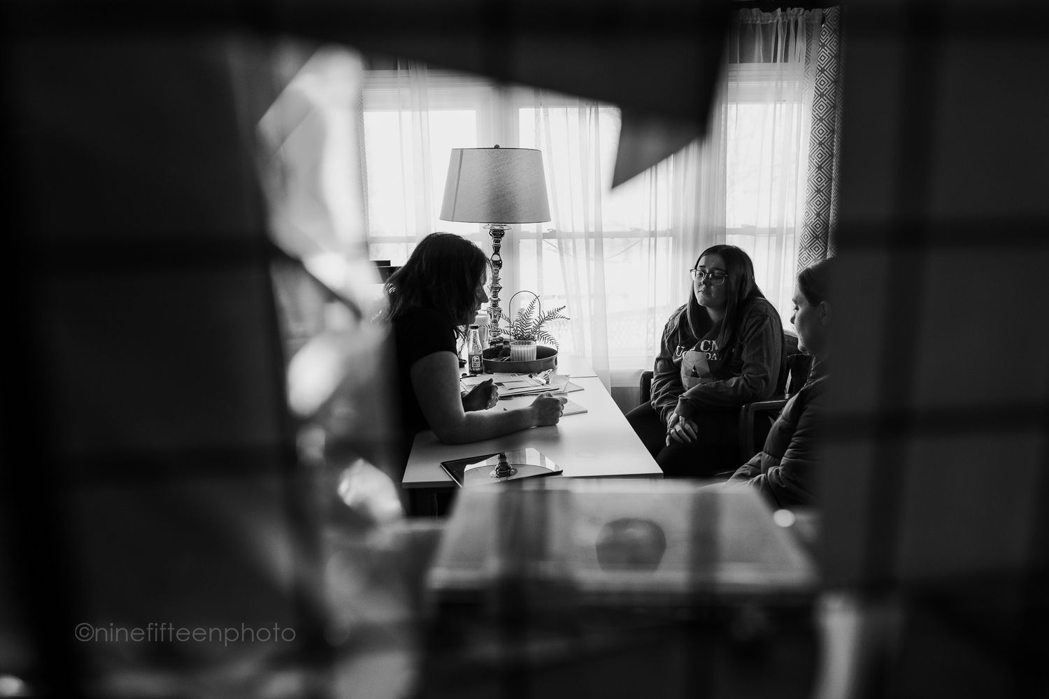 Black and white photo of women consulting at dining table in softly lit home interior.