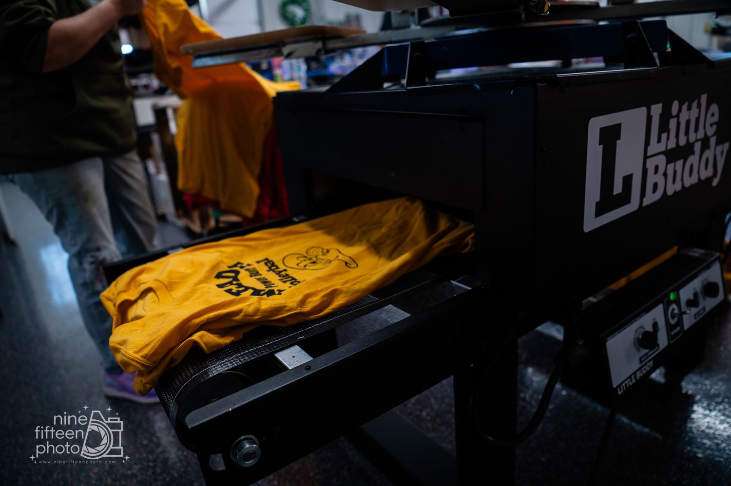 Yellow printed t-shirt lying on a Little Buddy conveyor dryer in a screen printing shop.