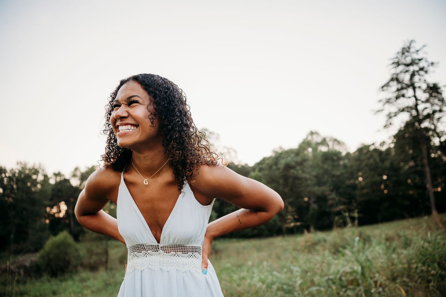 Outdoor senior portraits in Brandenburg KY with Bella in white dress laughing in open field by ninefifteenphoto