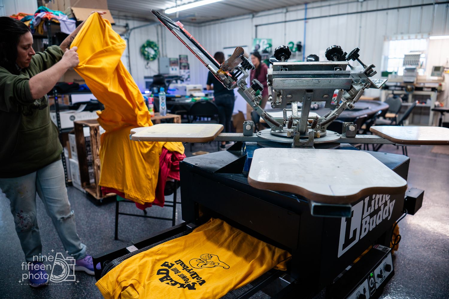 Worker pulling yellow shirt from screen printing press at MC Screen Printing in Brandenburg Kentucky.