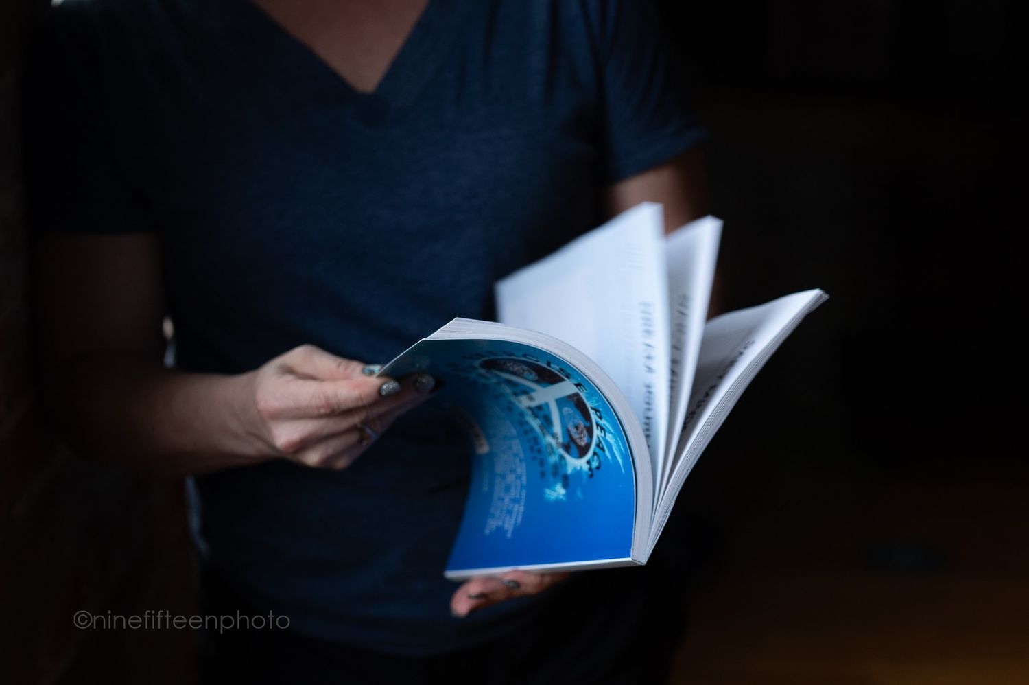 Person holding open book with blue underwater photography in dimly lit setting.