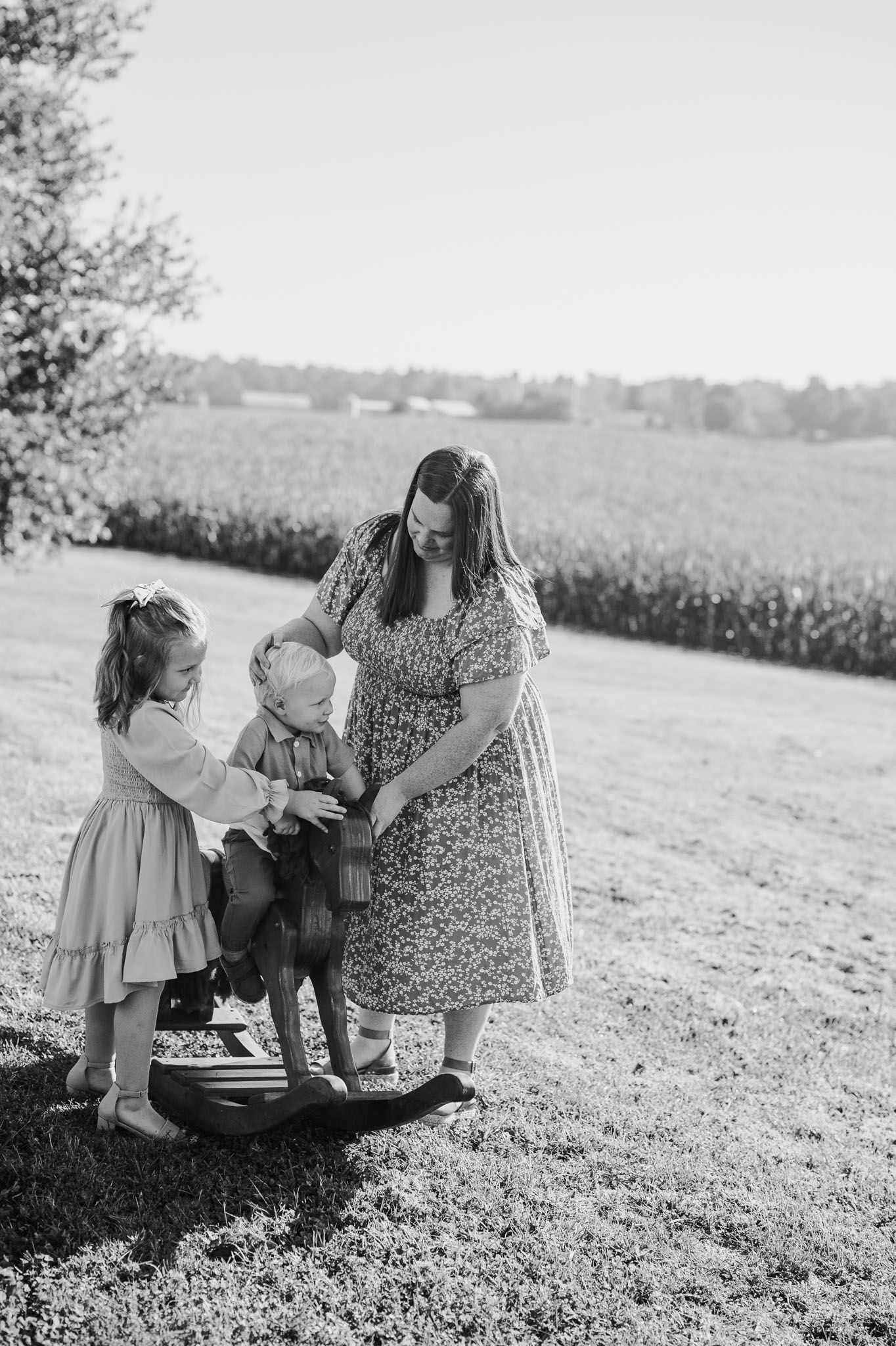 Timeless black and white candid of parents and child sharing a quiet moment in open field.