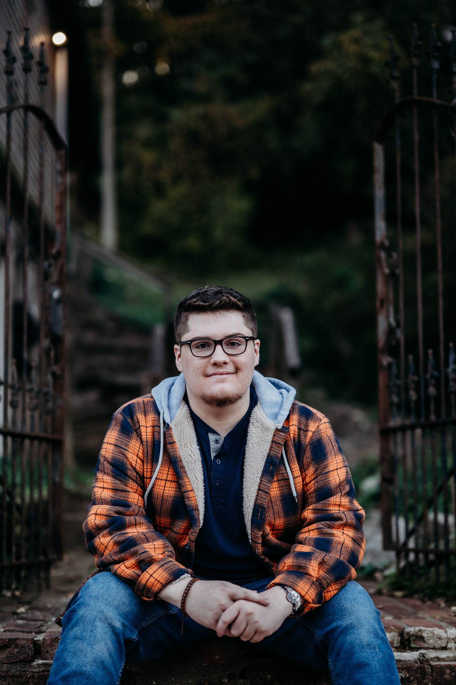 Luca sitting on stairs in his orange flannel smiling during his Brandenburg KY senior photo session.