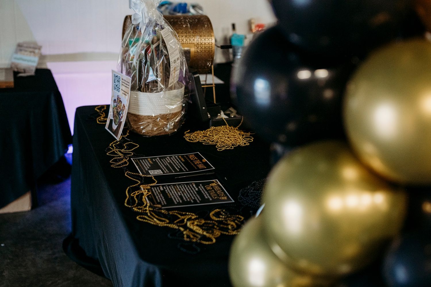 An elegant event table display with black and gold balloons, gift basket, and decorative accessories at a formal gathering.