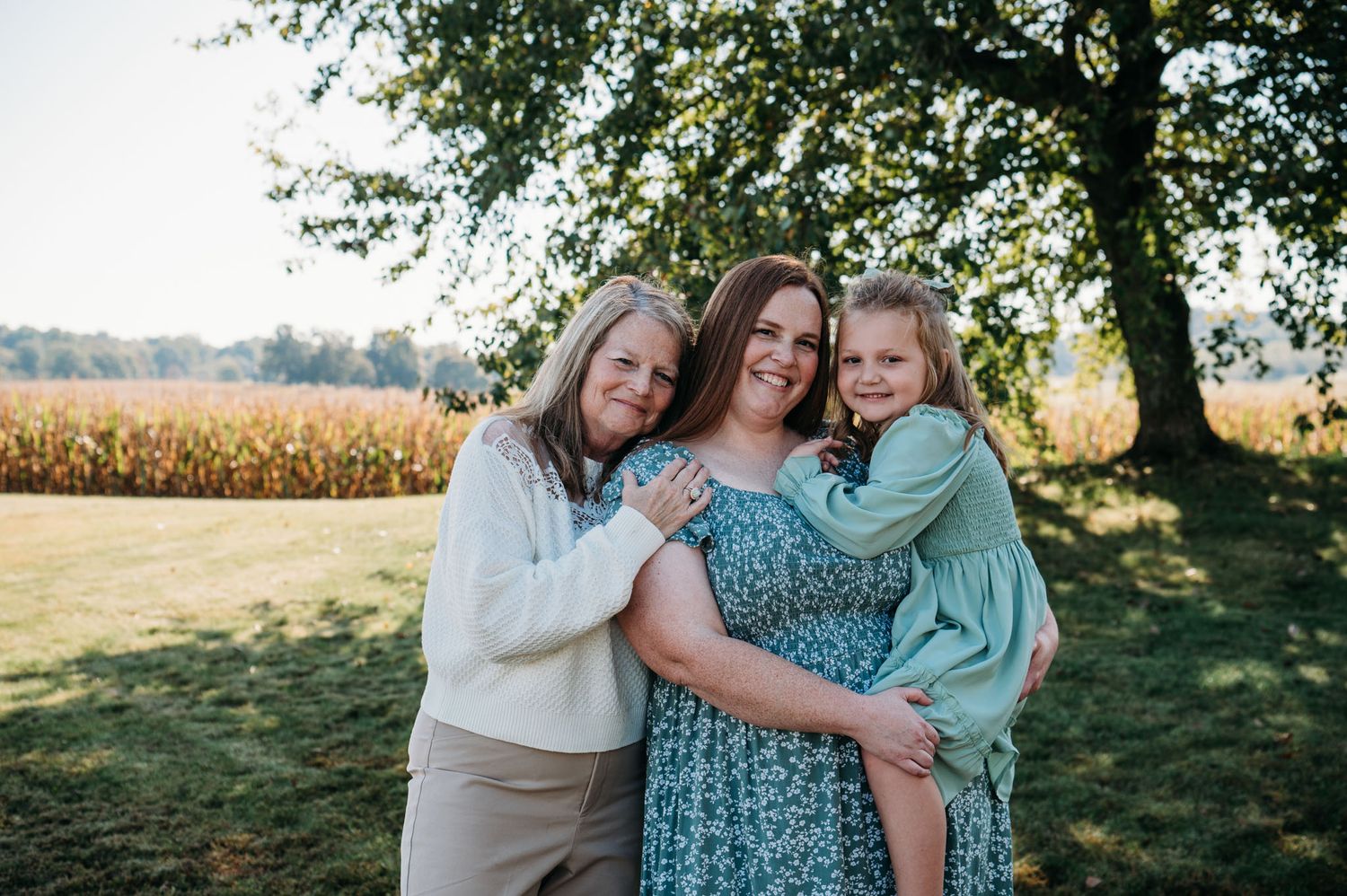 Three generations of women hugging under a tree in golden fall light during family photo session.