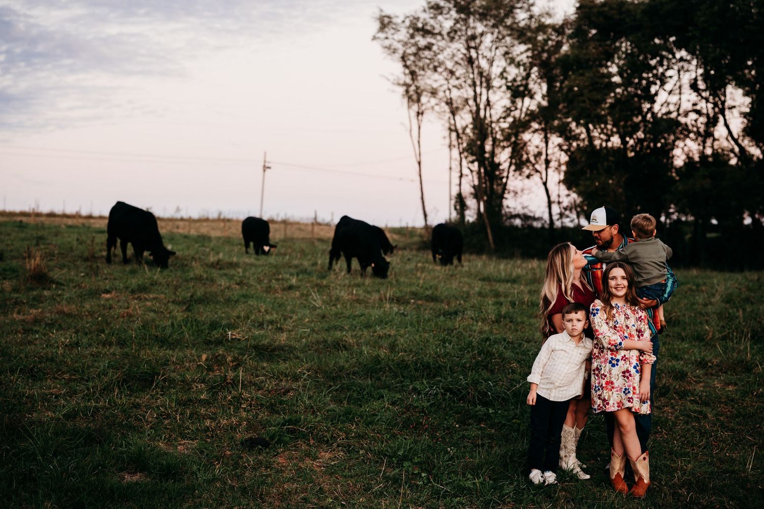 Family standing near cows in open pasture at dusk on their Guston Kentucky farm