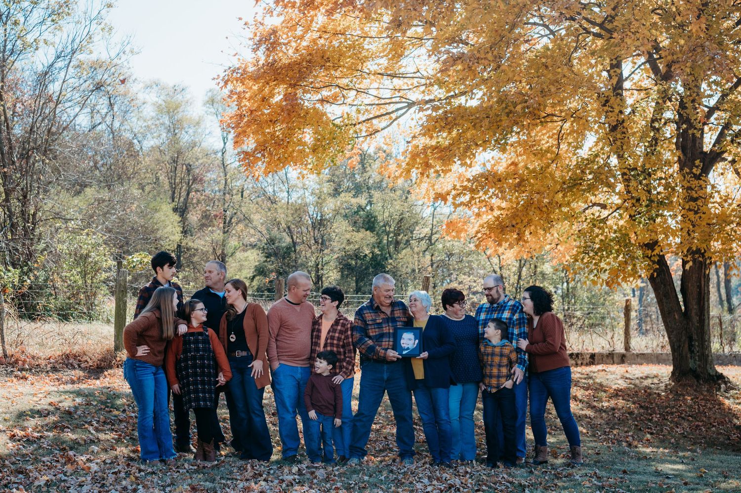 Large extended family gathering under colorful fall foliage trees for portrait.