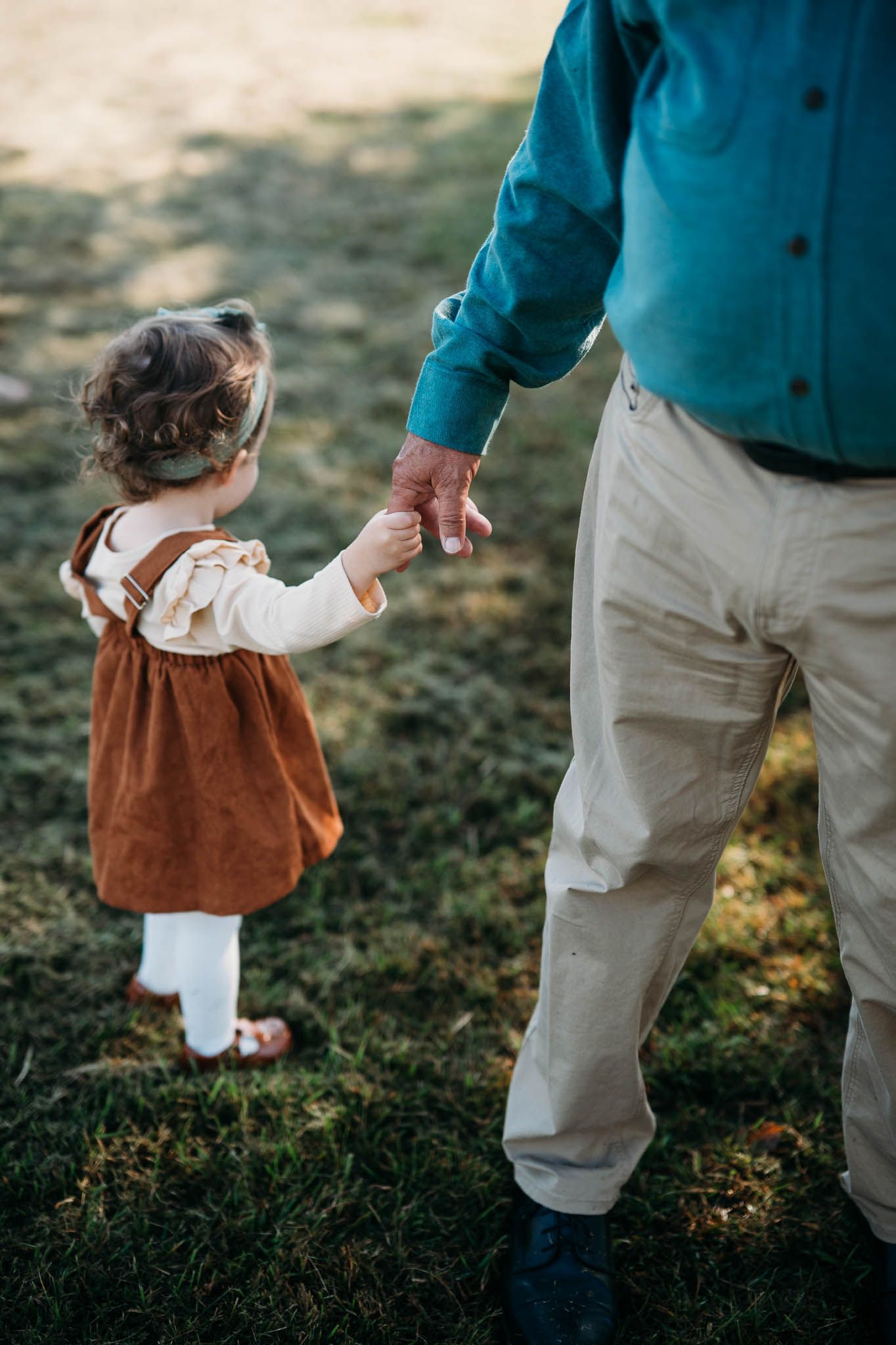 Grandfather walking hand in hand with toddler across sunlit fall field in Meade County Kentucky.