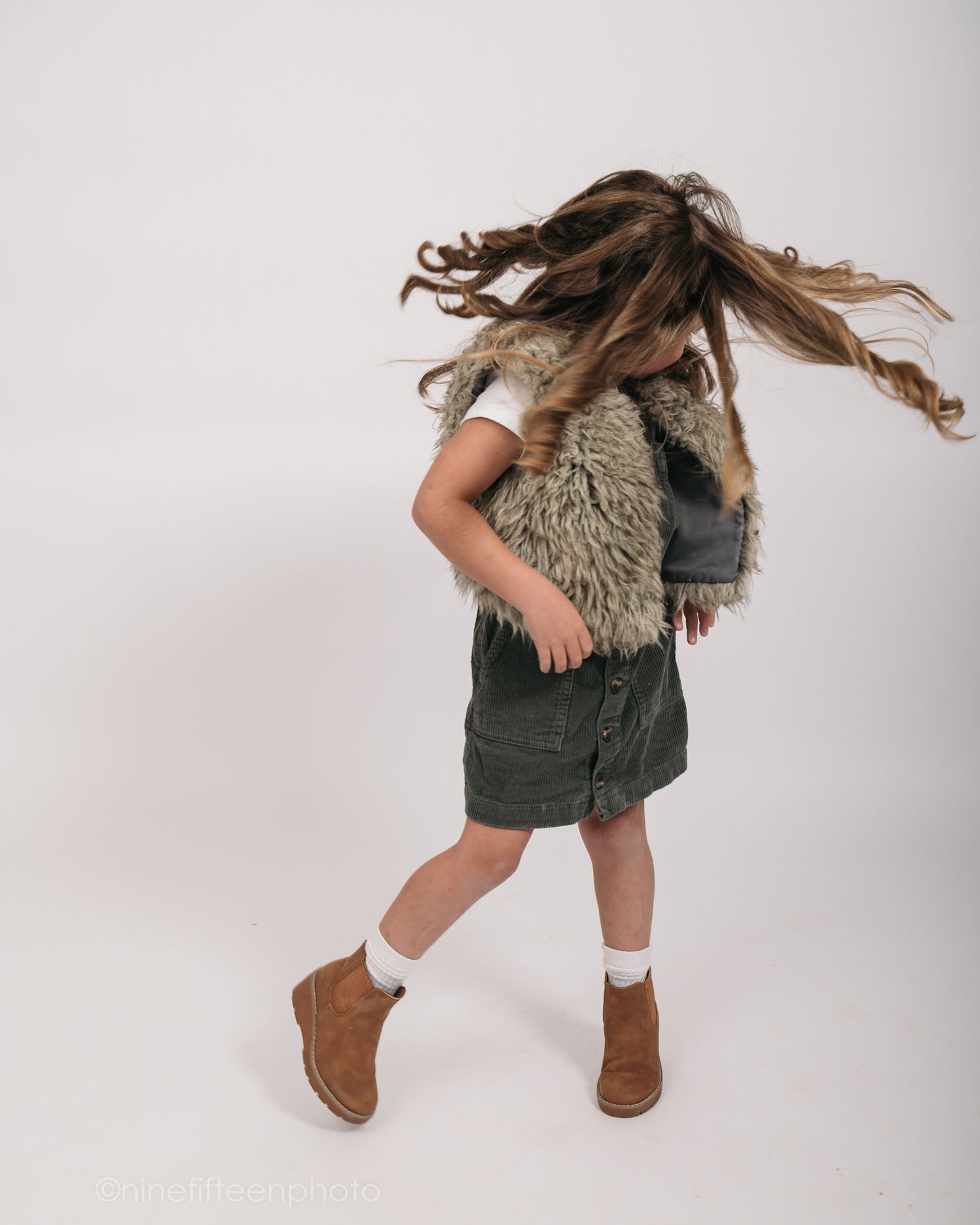 Studio personality portrait of a young girl smiling confidently in a textured vest against a neutral studio backdrop in Meade County KY