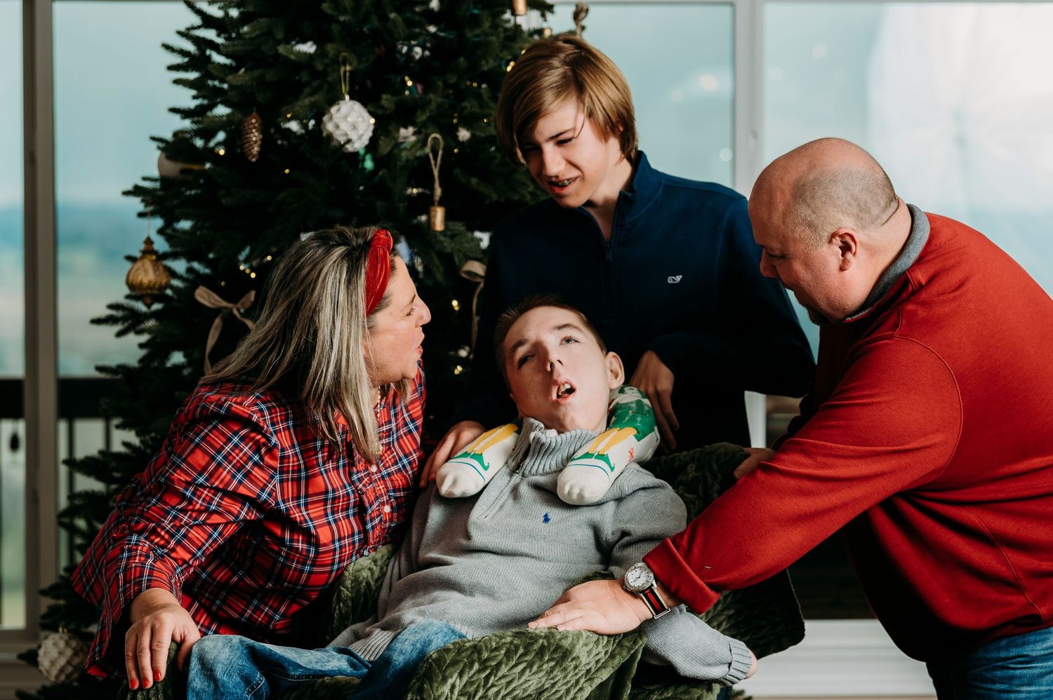 Family gathered around child near Christmas tree in festive holiday portrait.