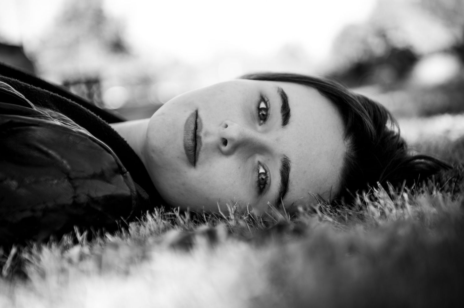 Black and white portrait of young woman lying on grass looking at camera.