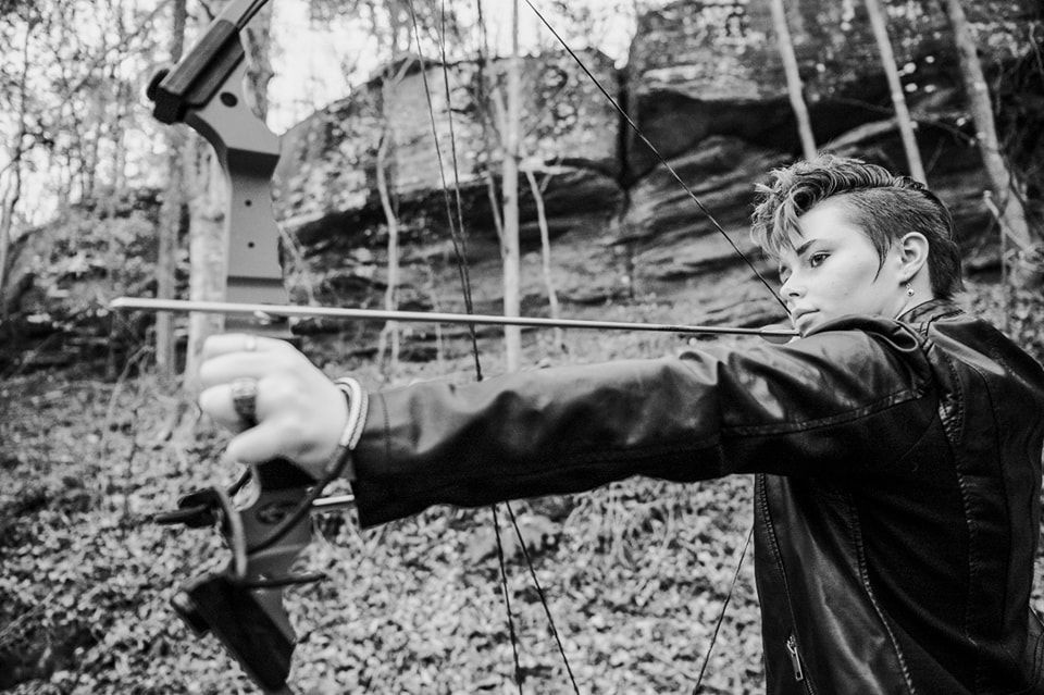 senior in a black and white photo holding her bow and arrow during the session with ninefifteenphoto
