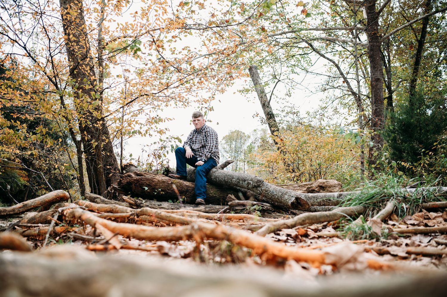 Mayson sits among fall leaves during his outdoor senior photos in Brandenburg KY