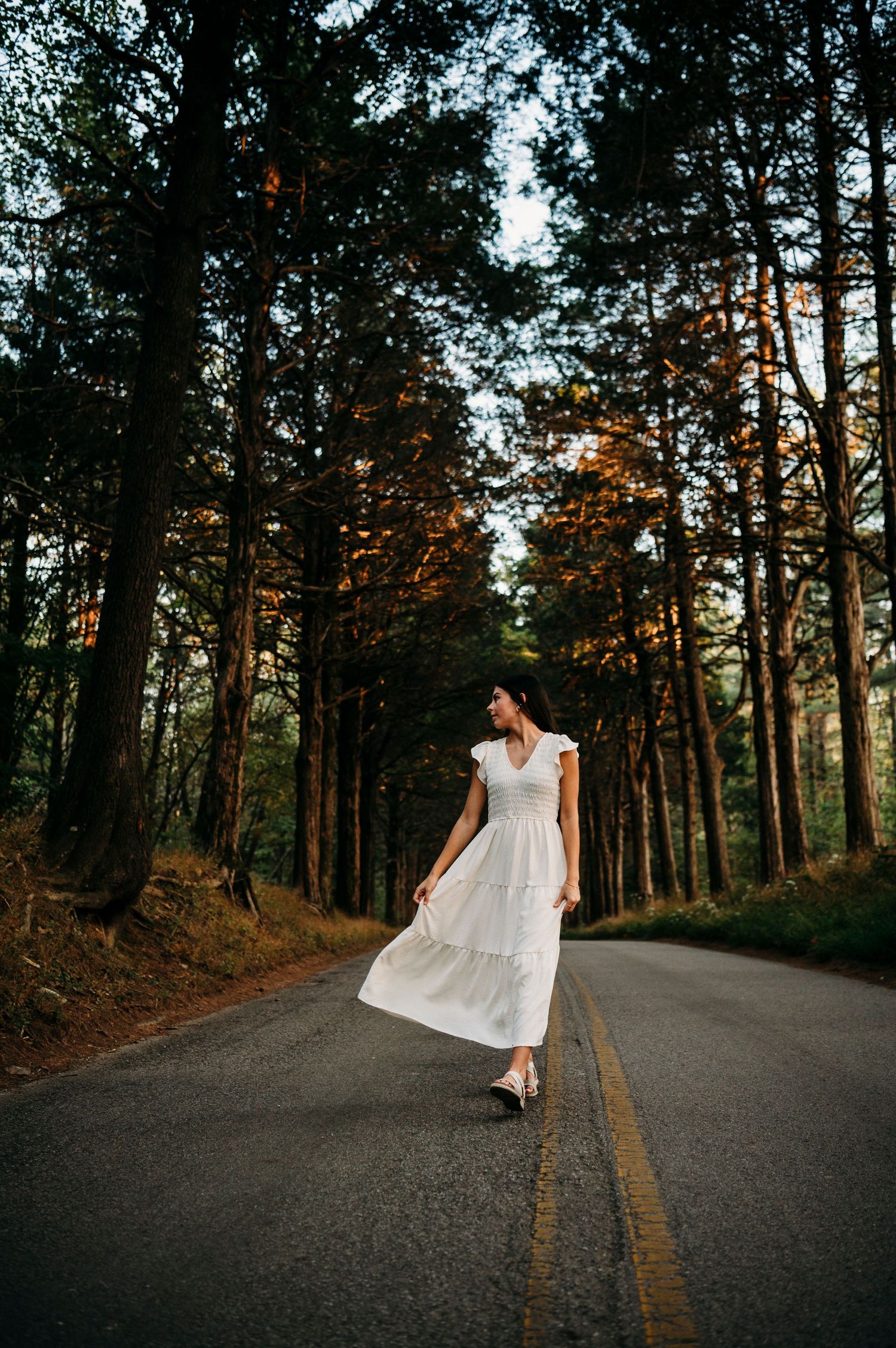 Emily walking down a quiet tree-lined road in Brandenburg KY during her senior photo session by ninefifteenphoto.
