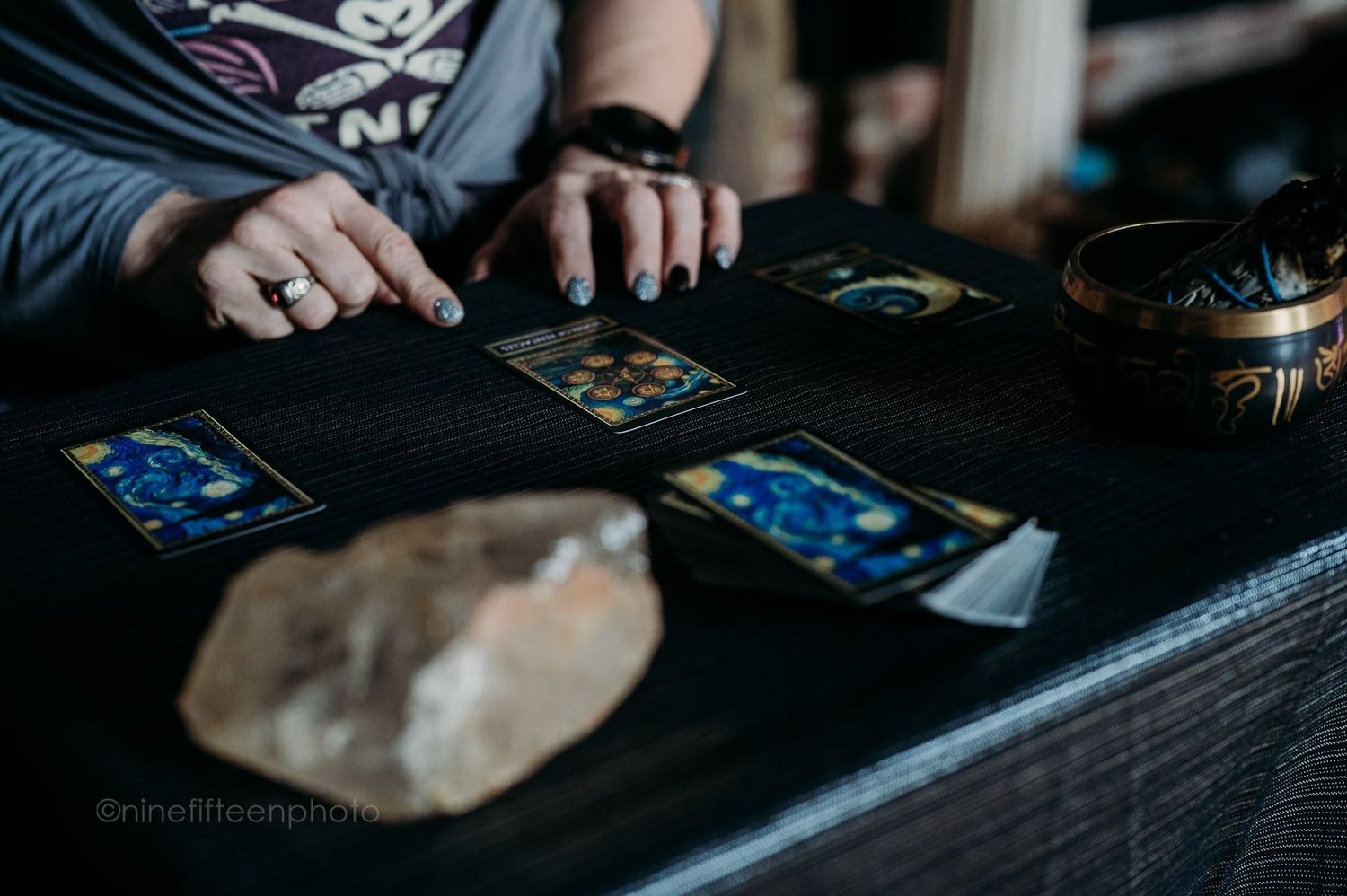 Hands with rings arrange tarot cards on dark cloth with crystals during a reading session.