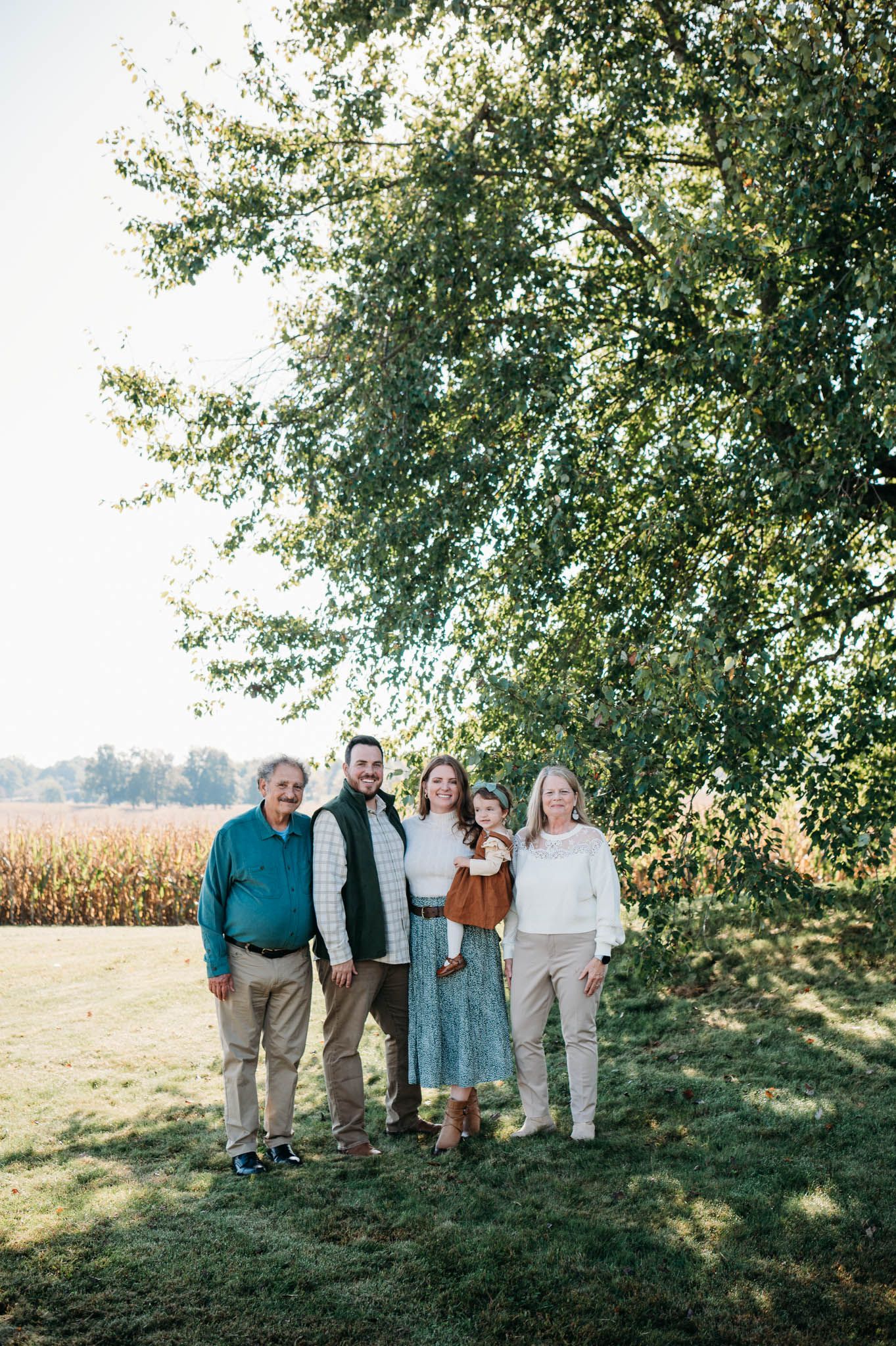 Three generations of family standing together beneath a tree in warm golden light in Brandenburg Kentucky.