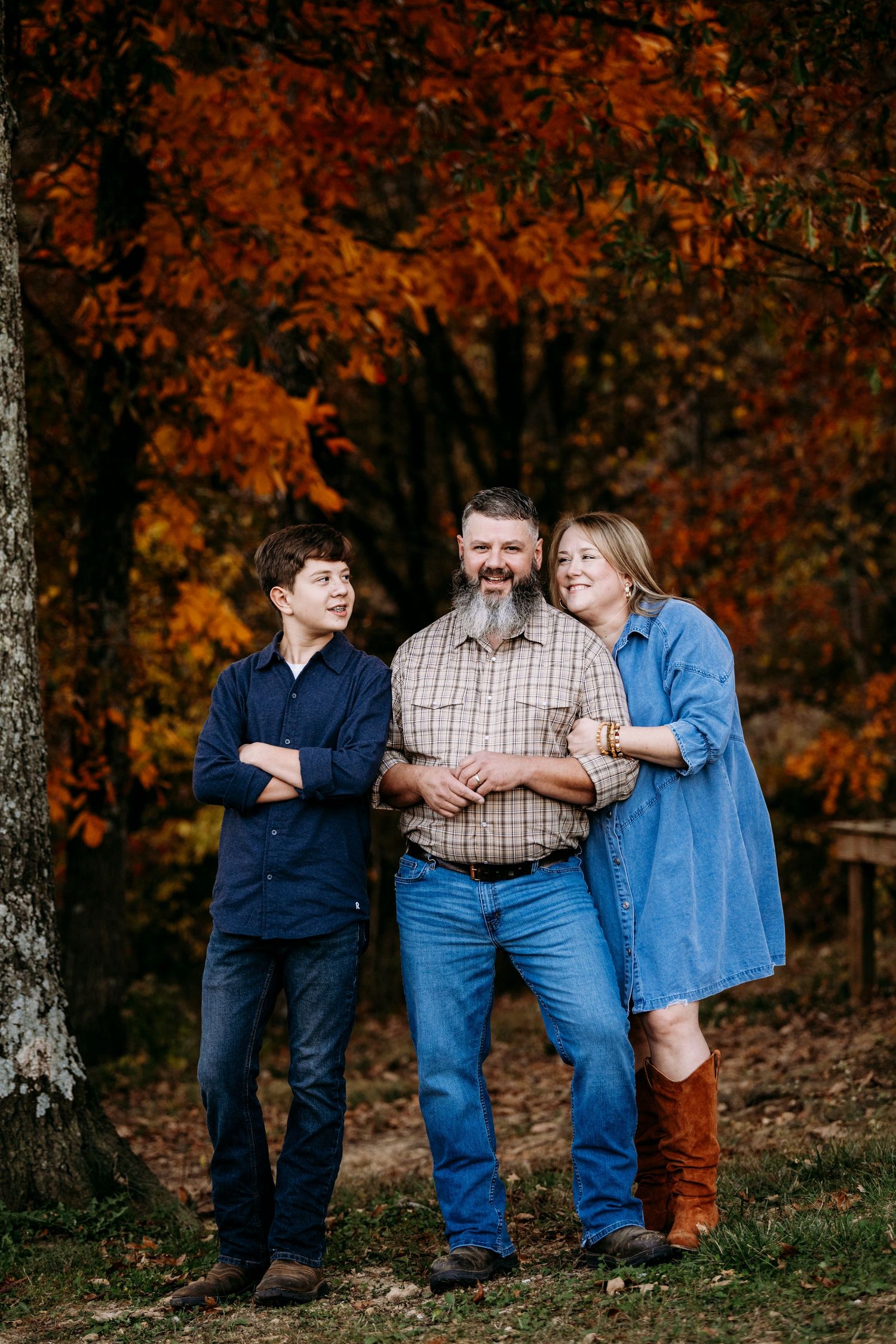 Father with son and daughter posing before vibrant red autumn foliage trees.