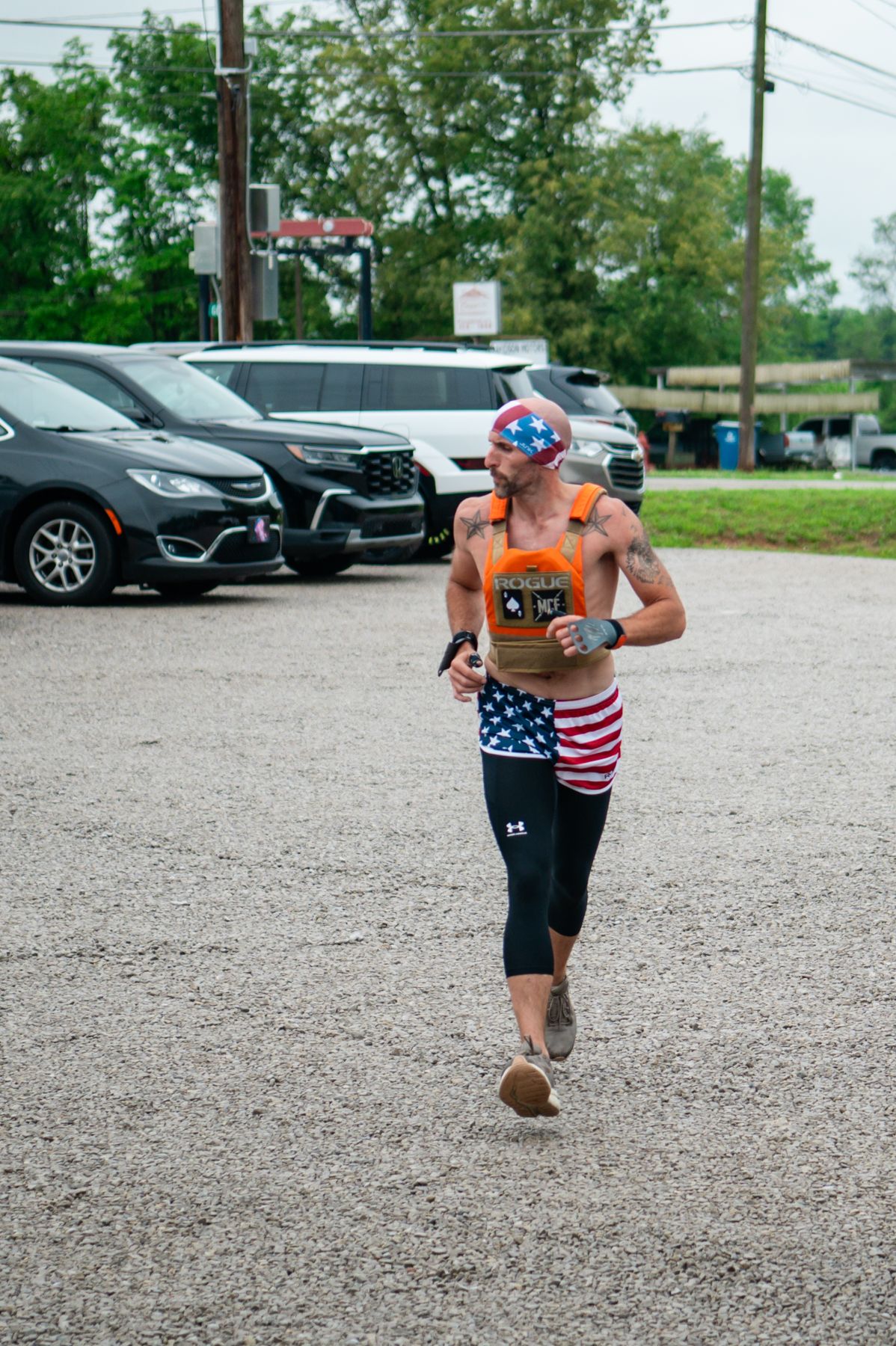 Athlete running in American flag shorts and patriotic bandana during outdoor race event in parking lot.