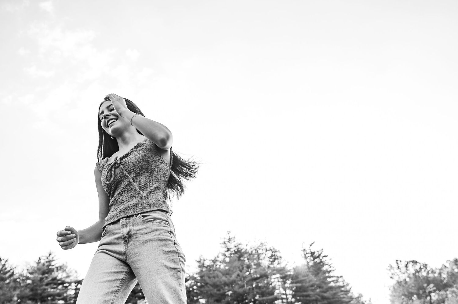 Black and white photo of Emily in jeans smiling in the sunlight during her Otter Creek Park senior session.