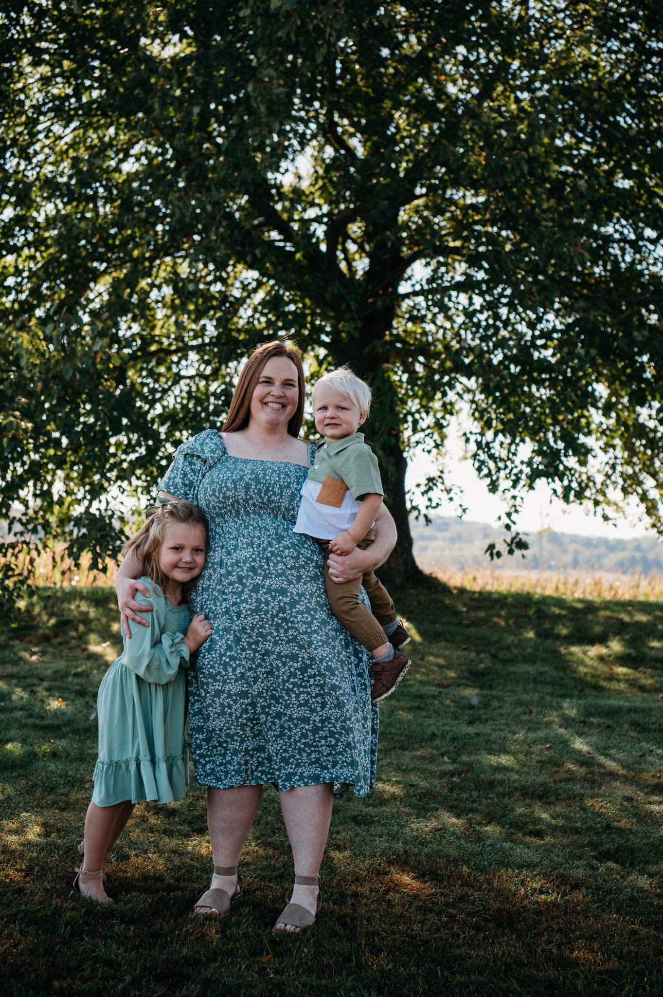 Parents holding toddler under a tree during outdoor fall photo session in Brandenburg Kentucky.