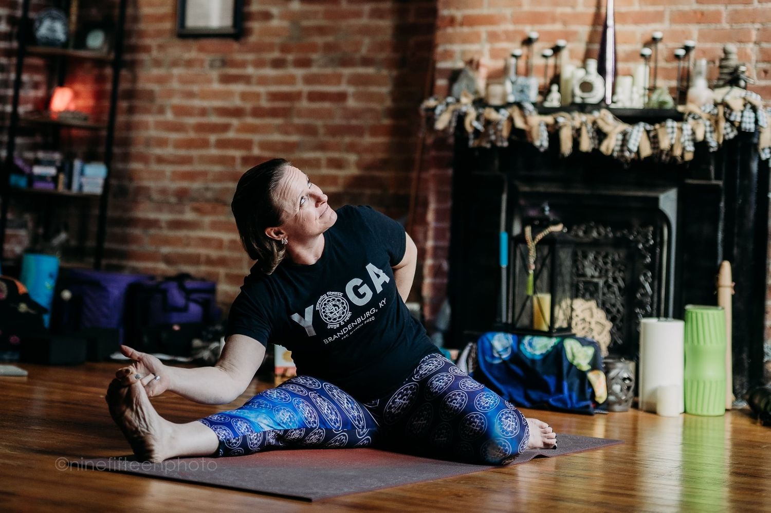 Woman in yoga attire doing a seated spinal twist stretch on a mat in a cozy studio.