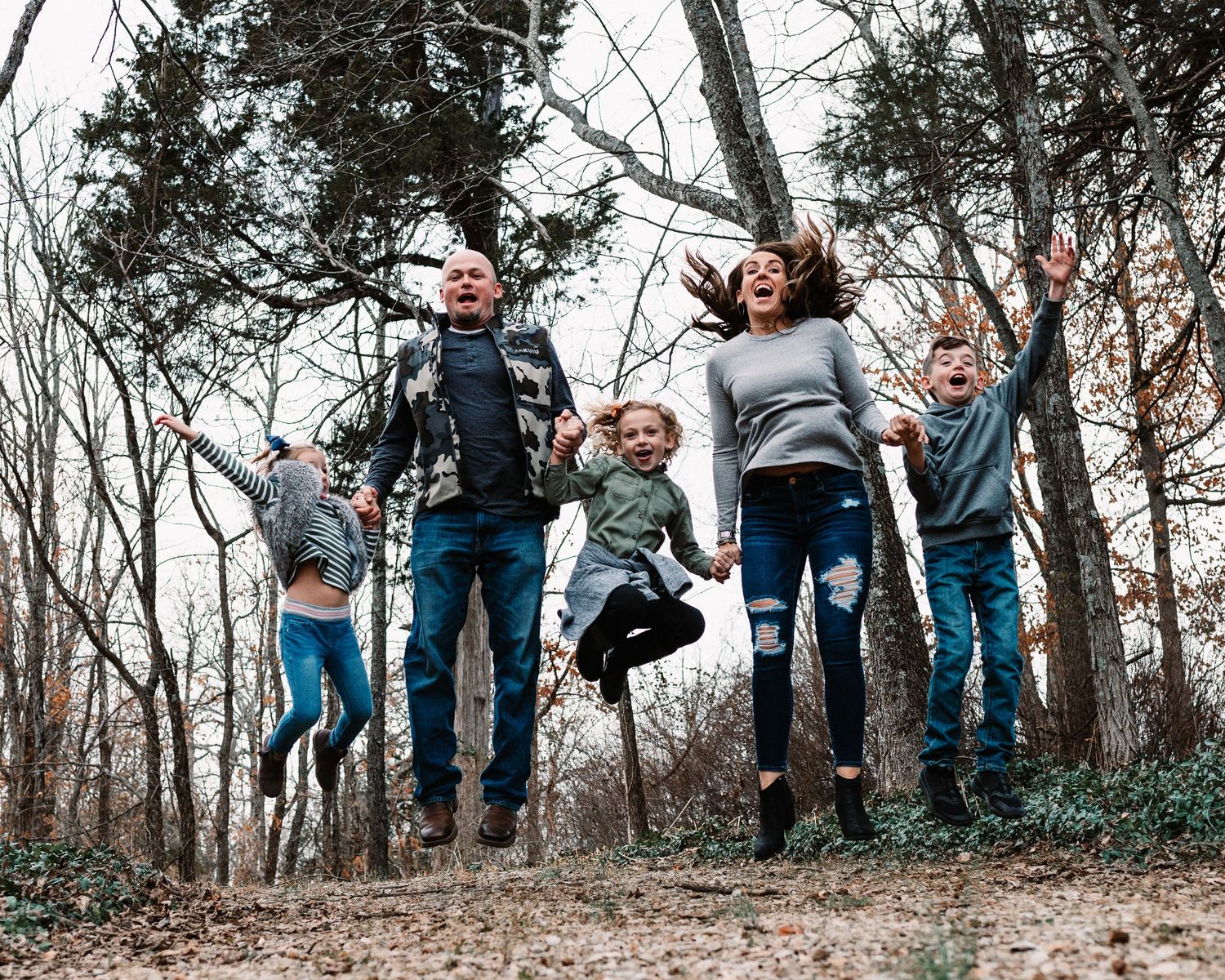 Joyful family of five jumping together in wooded outdoor fall setting.