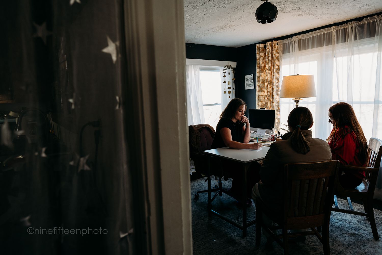Three women sitting at dining table near window in star-decorated room during consultation.