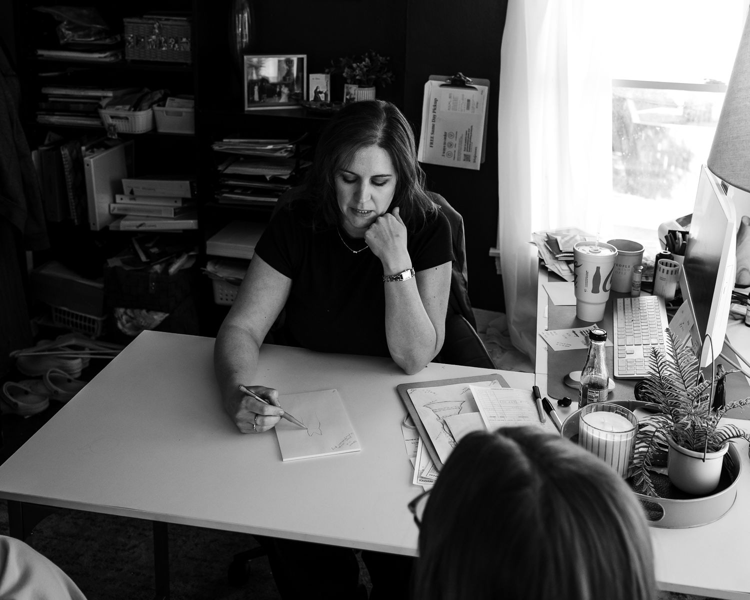 Woman in black top reviewing documents at a desk in a cozy office, black and white photo.