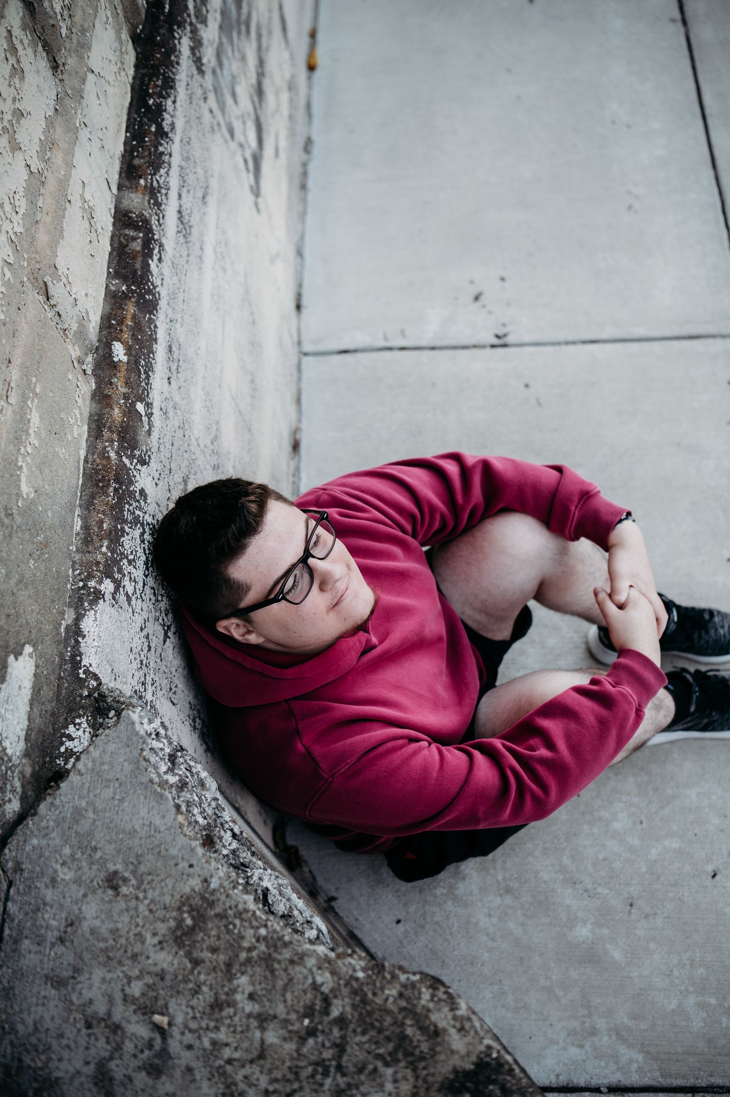 Luca’s senior photo in downtown Brandenburg KY wearing a red hoodie, sitting on steps and smiling.