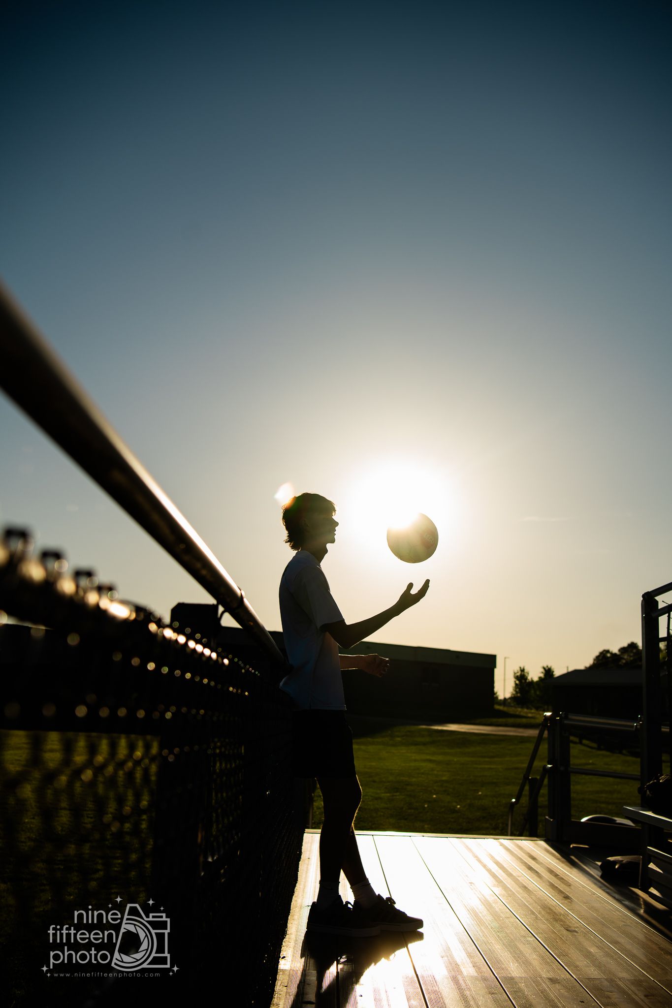 Silhouette of a person tossing a volleyball at sunset on a wooden deck, backlit by golden sun.