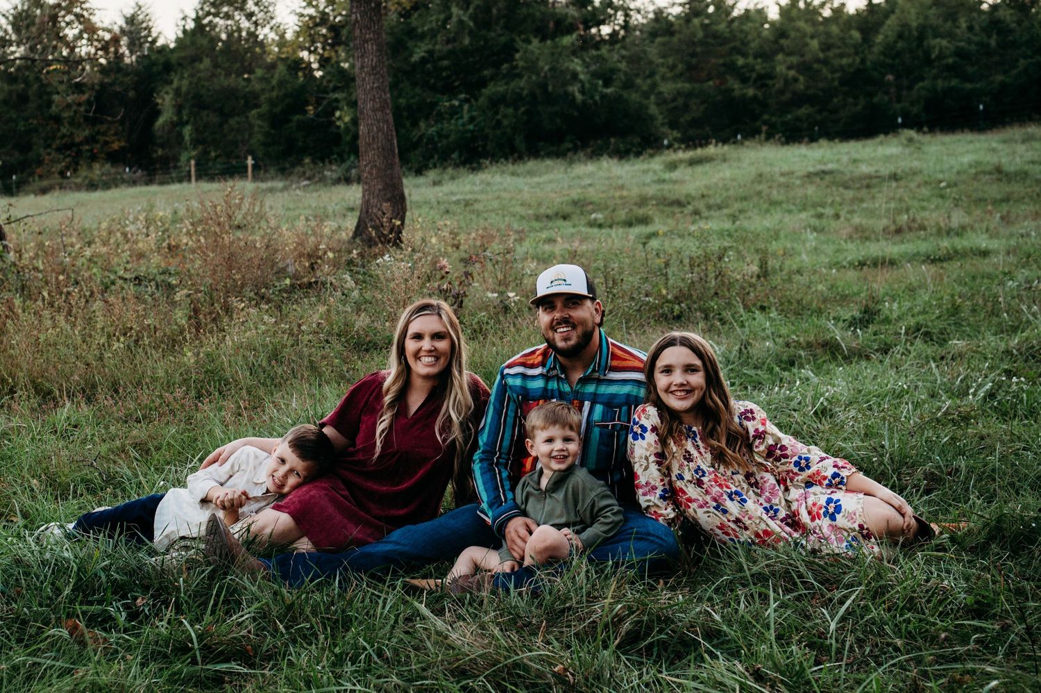 Family sitting together in grassy field under trees at sunset in Guston Kentucky