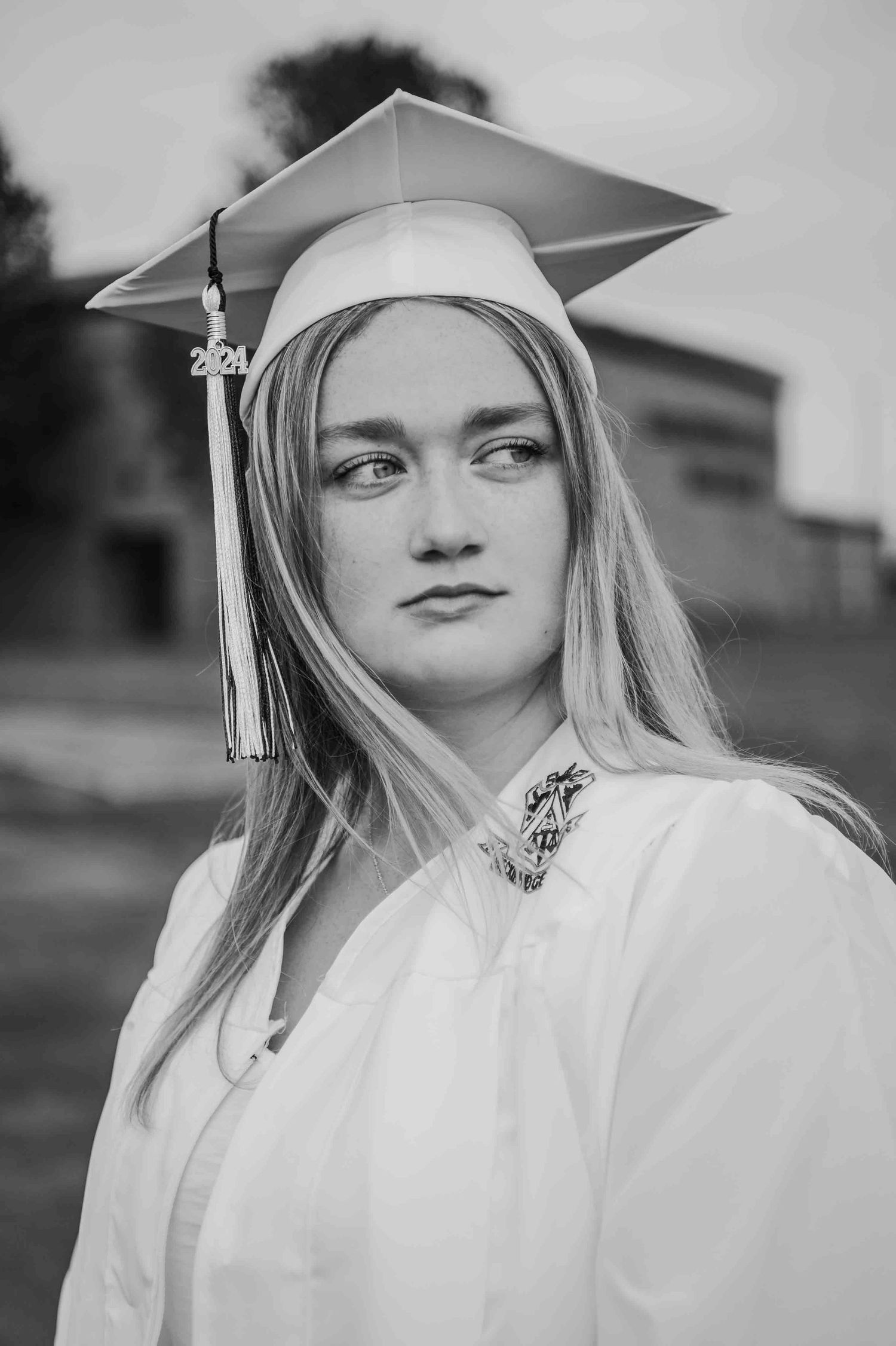 Black and white portrait of a young woman in graduation cap and gown with 2021 tassel outdoors.