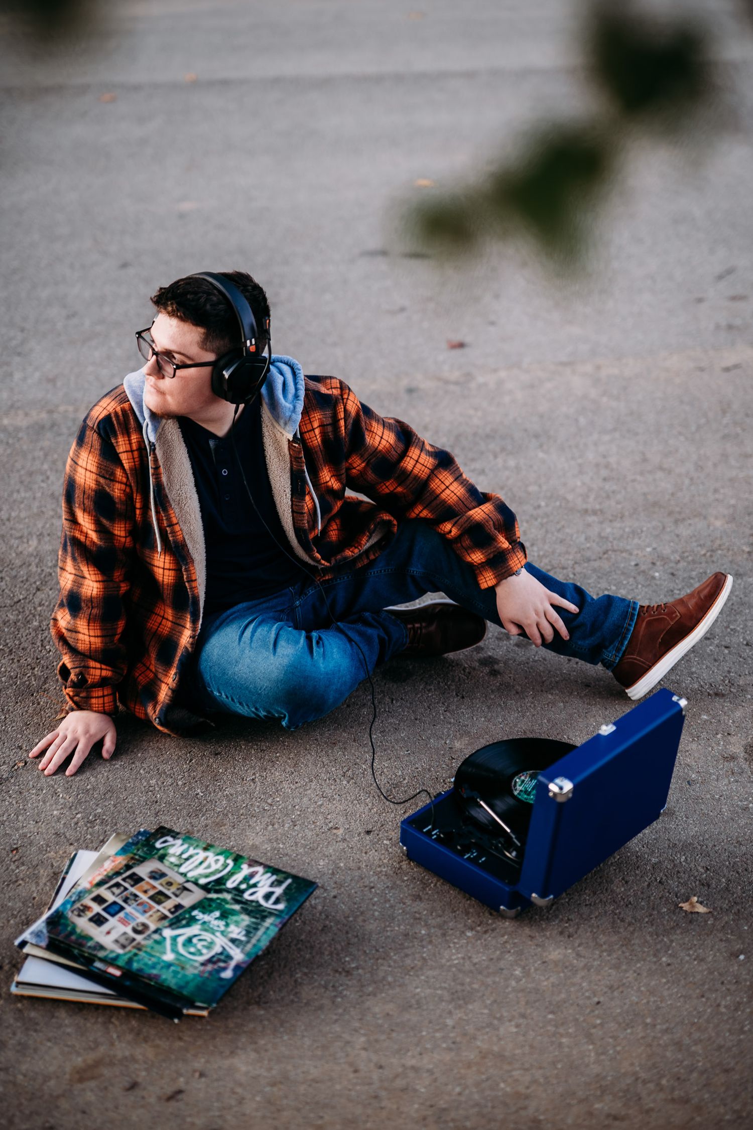 Luca sitting on the pavement in his orange flannel with a blue record player and vinyls during his senior session.