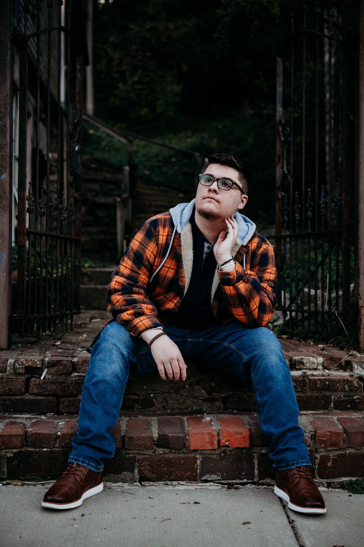 Luca sitting on brick steps downtown wearing an orange flannel during his senior photo session in Brandenburg KY.