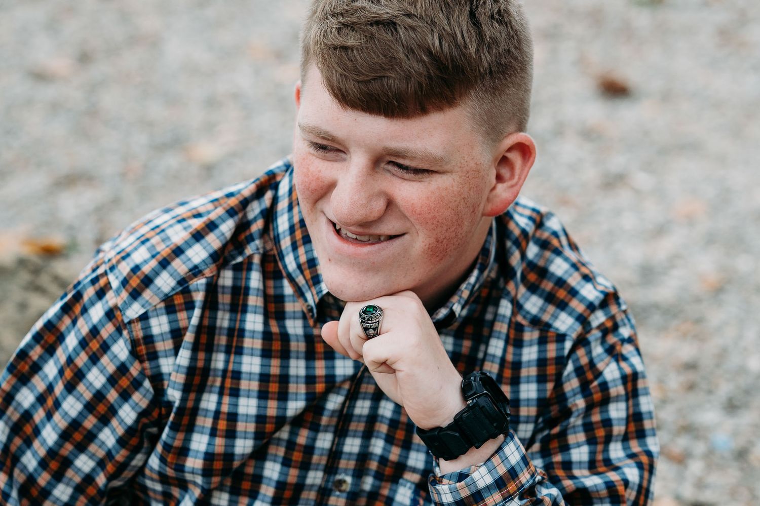 Smiling young man in plaid shirt resting chin on hand with autumn leaves in the background.