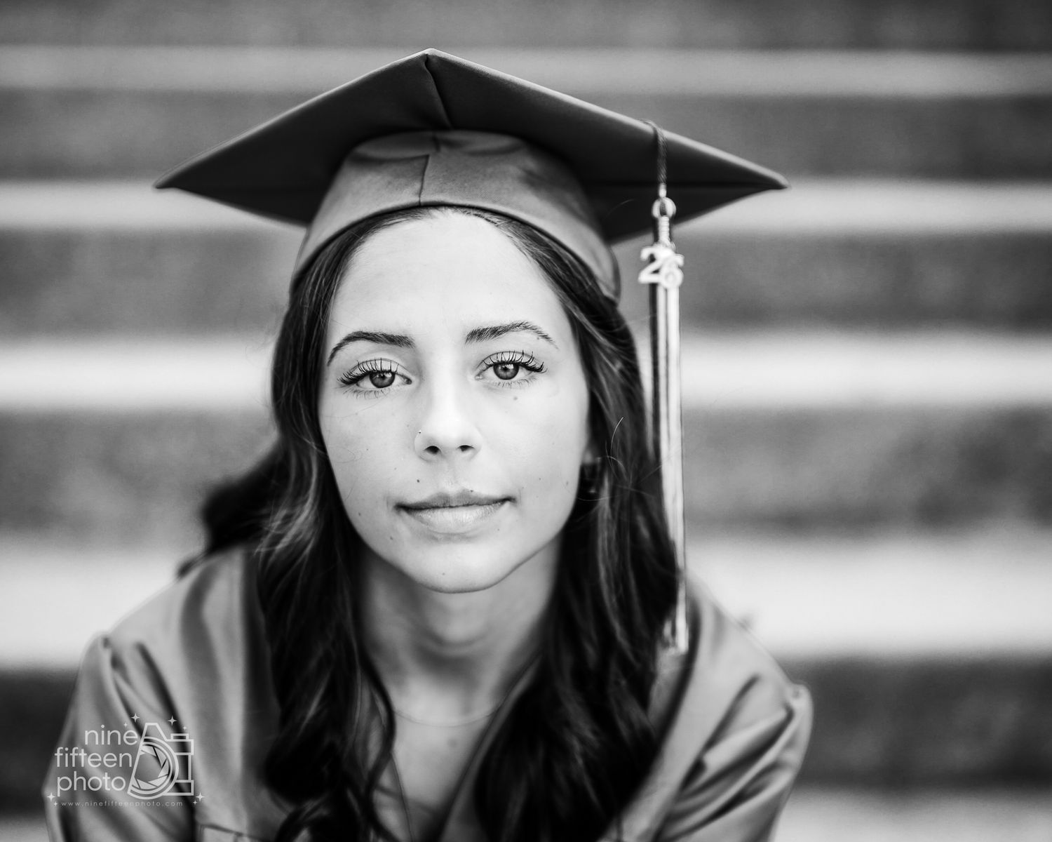 Black and white close-up portrait of a young woman in graduation cap and gown on steps.