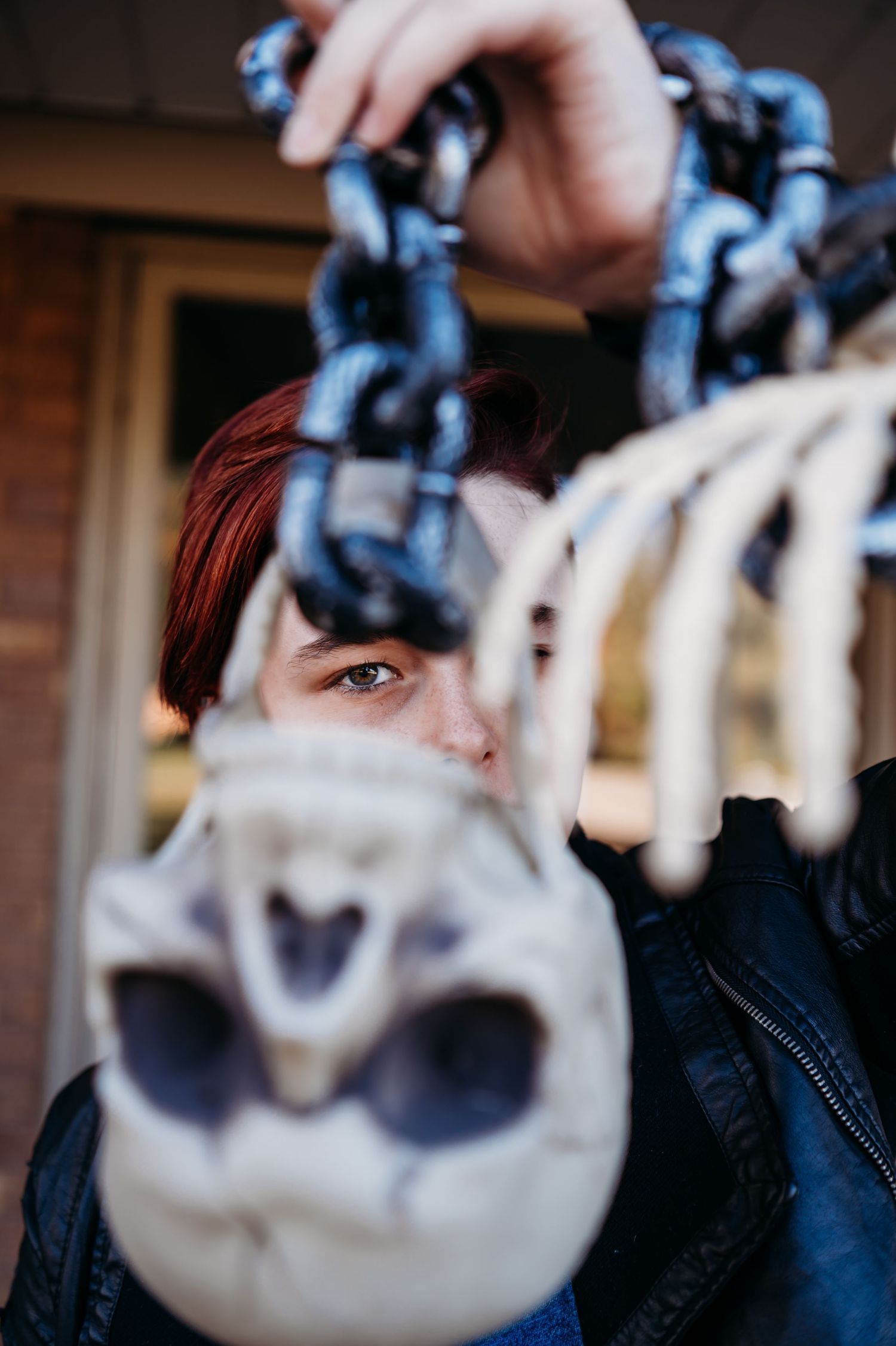 Person with red hair holding skeleton and chains toward camera outdoors.