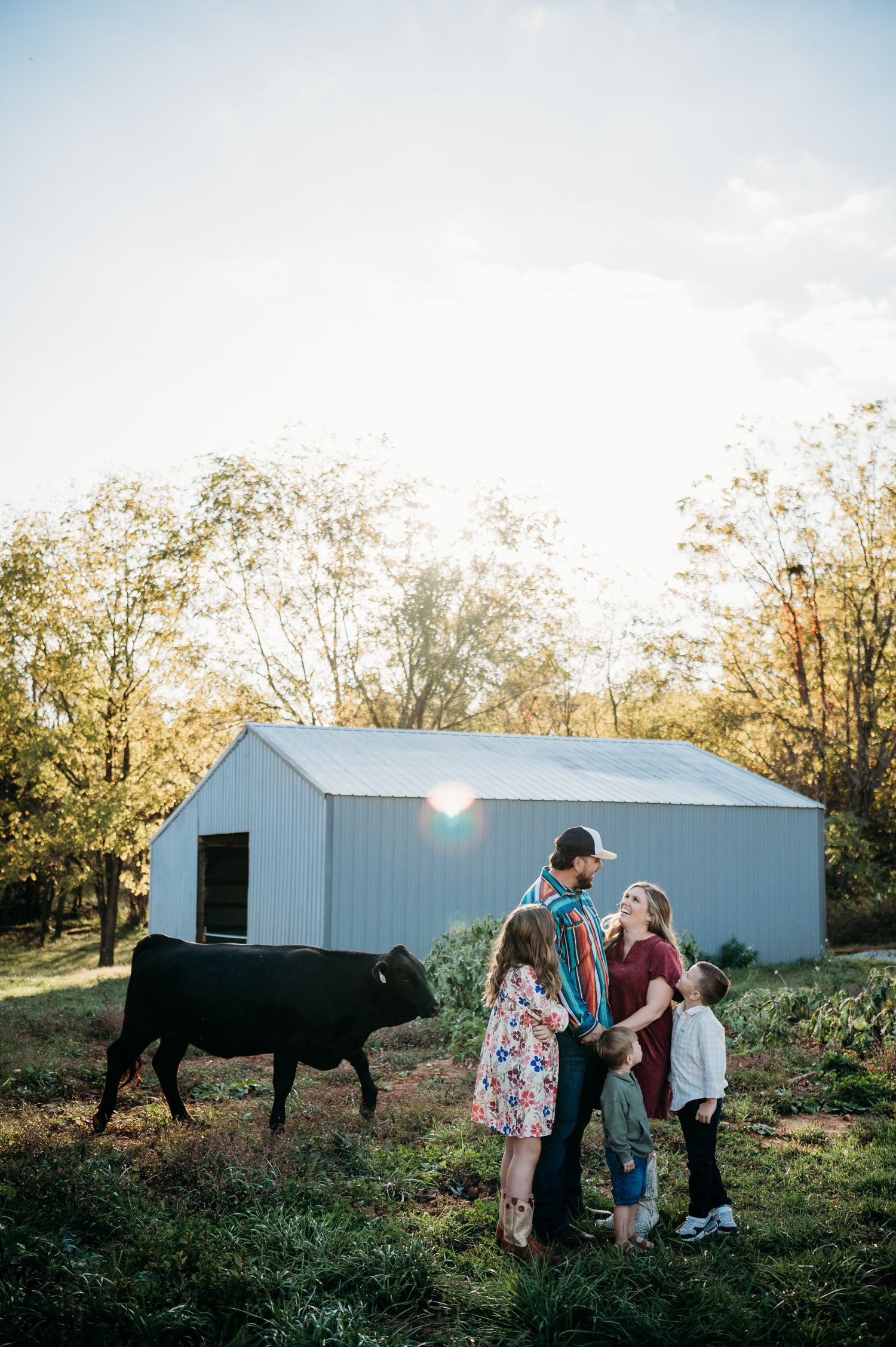 Family smiling near barn with cow in Guston Kentucky during golden hour, captured by ninefifteenphoto