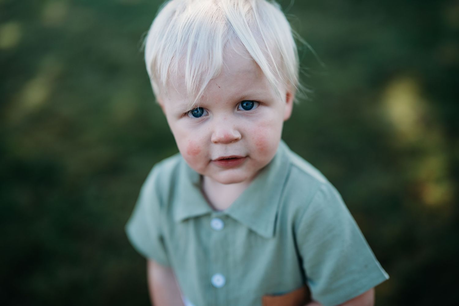 Close-up of smiling blonde toddler in green shirt during outdoor family photo session in Brandenburg KY.