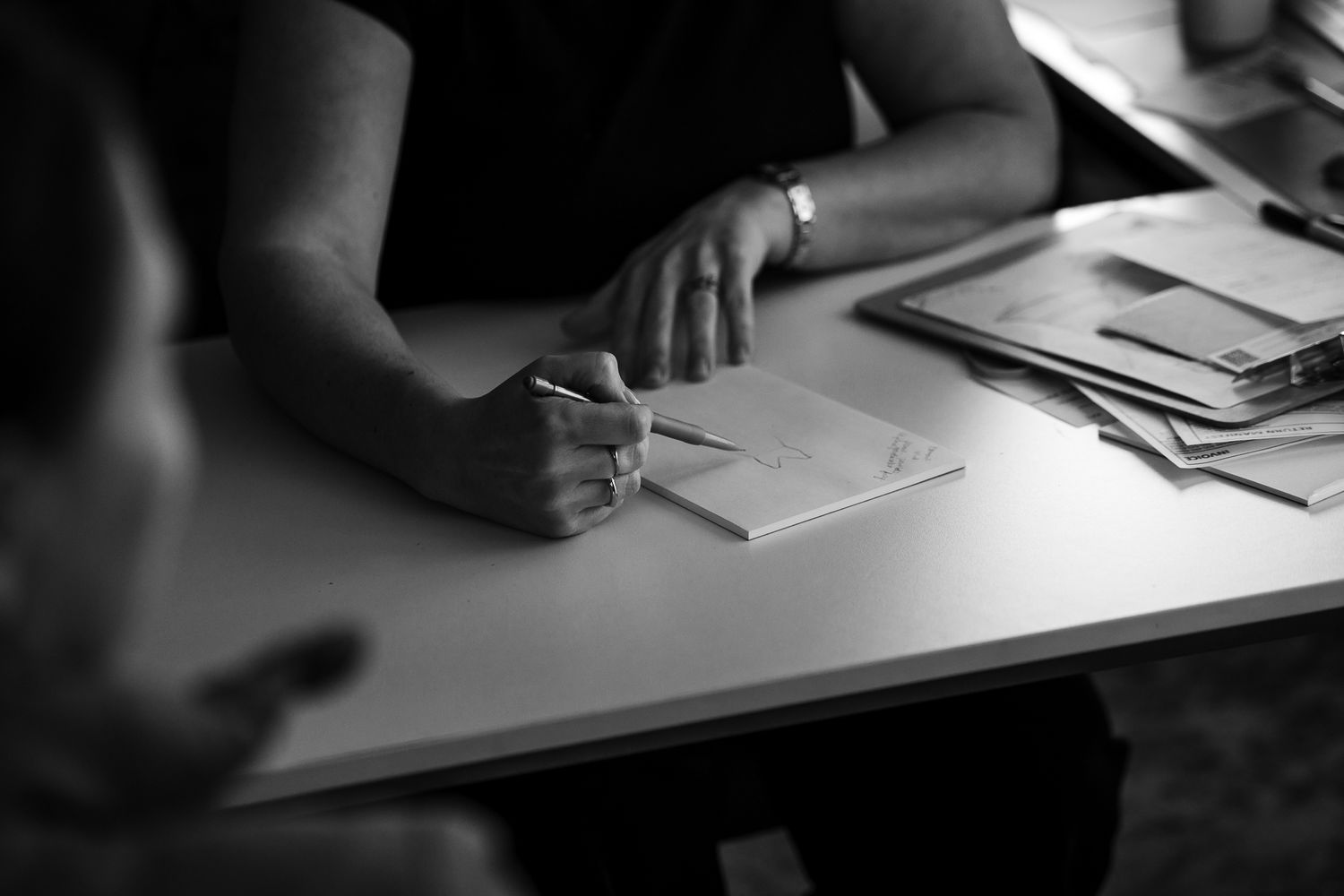 Close-up of hands writing notes on paper at a desk with documents, black and white photo.