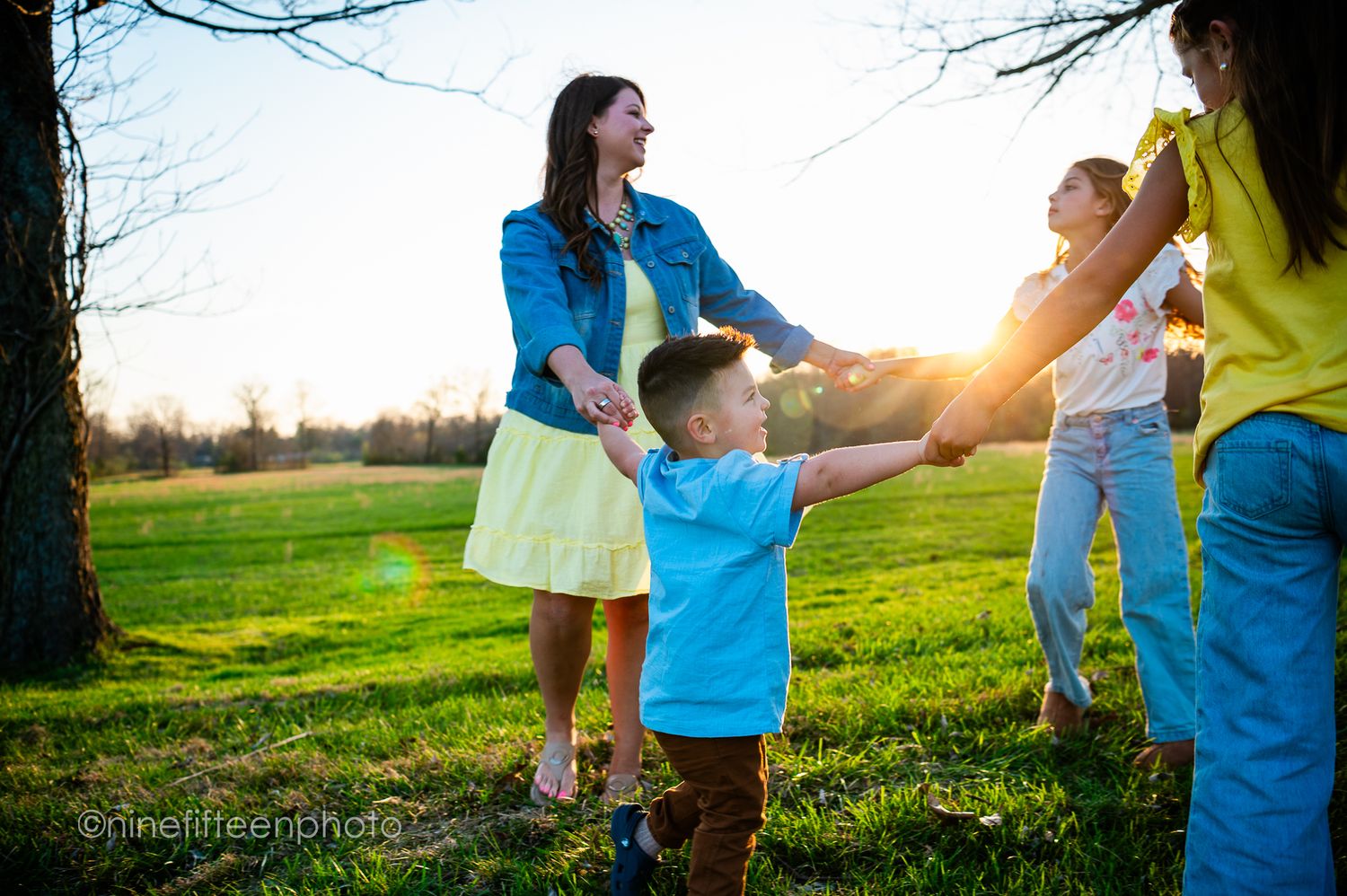 Joyful family playing ring-around-the-rosy in a sunny green park at golden hour sunset.