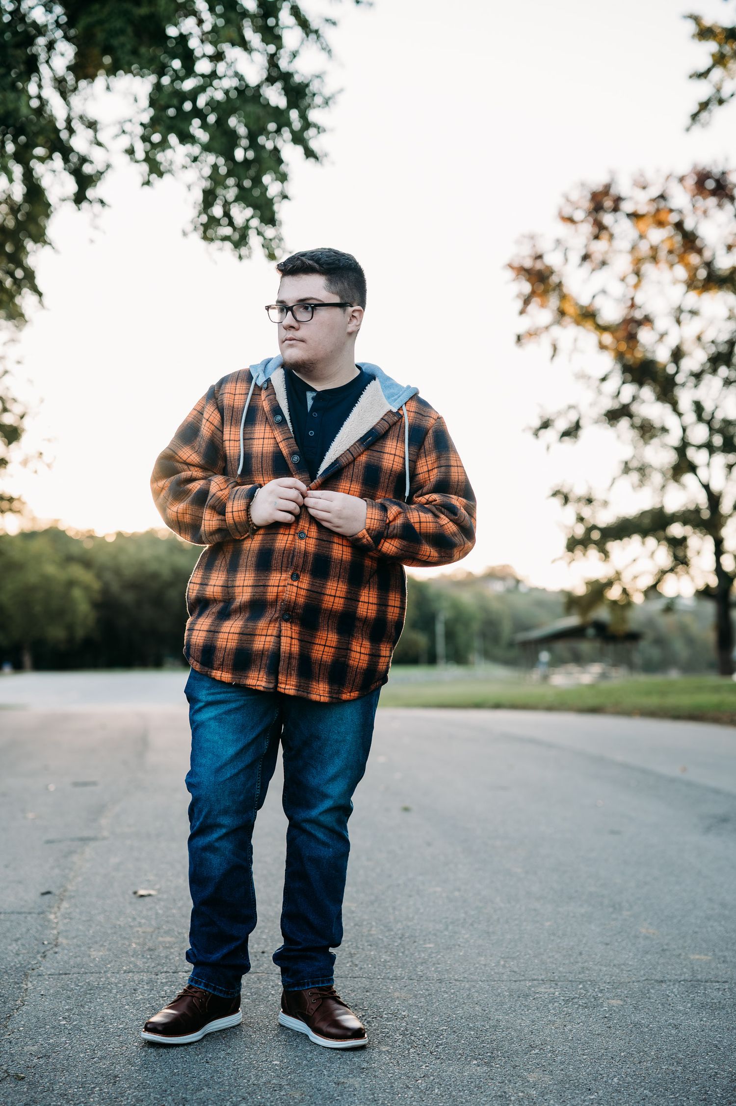 Luca standing in the street at sunset in orange flannel during his senior photo session in Brandenburg KY.
