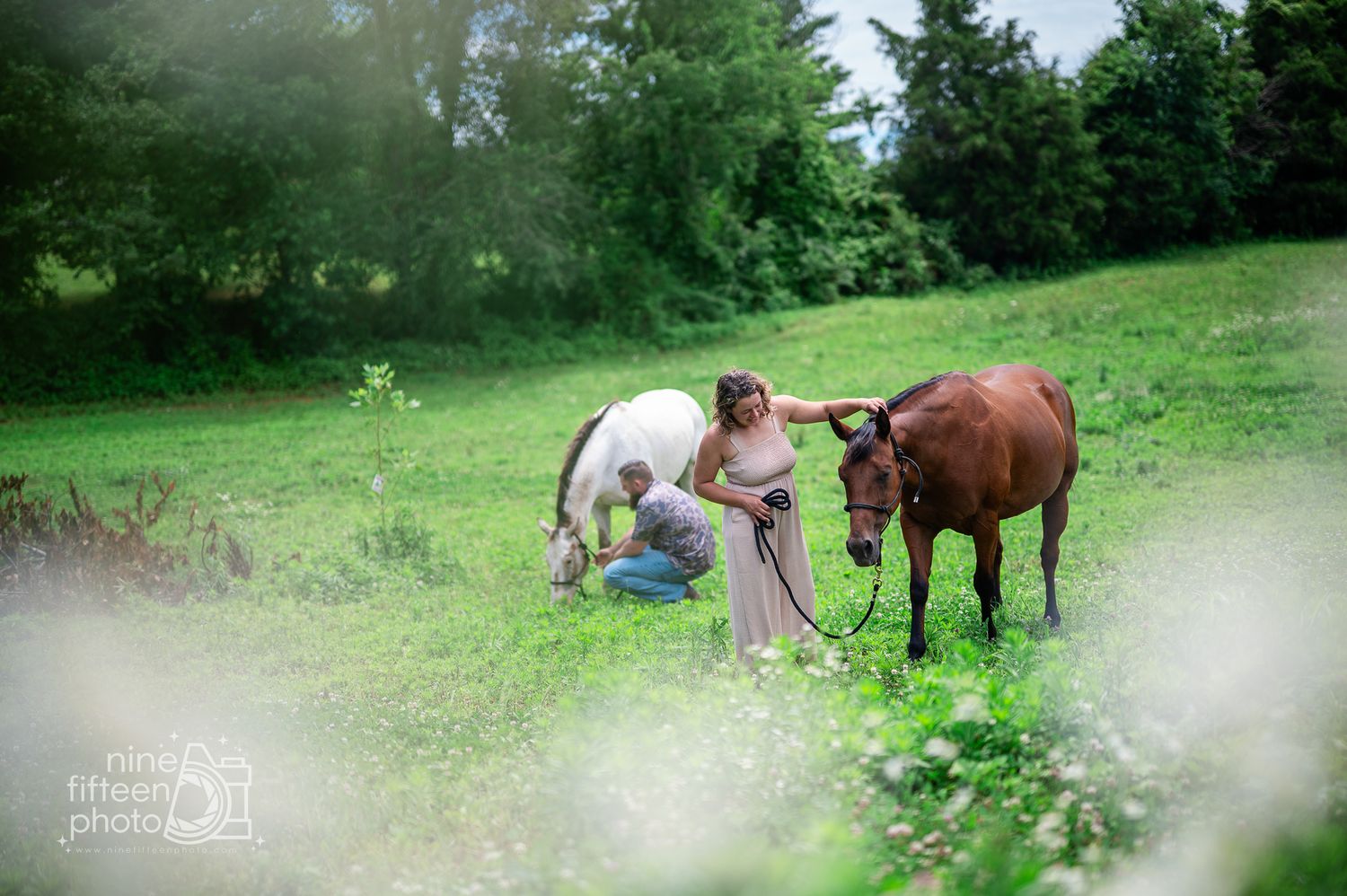 Two women interact with a white and brown horse in a lush green meadow during an outdoor equestrian photo session.