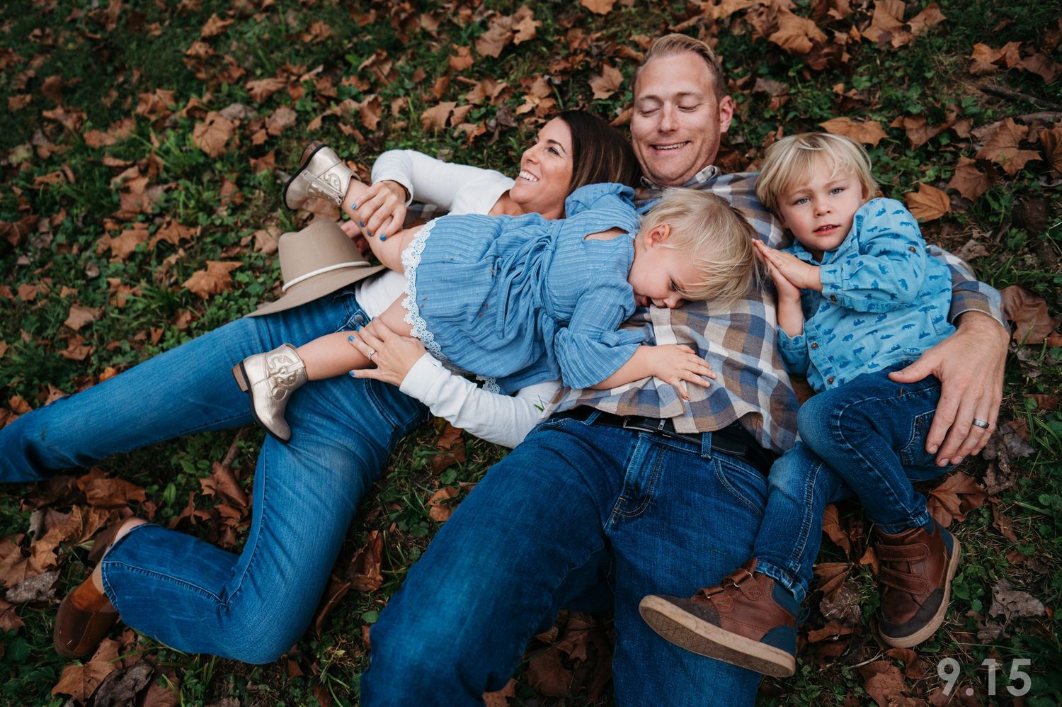 Family of four lying together on fall leaves laughing in outdoor portrait.
