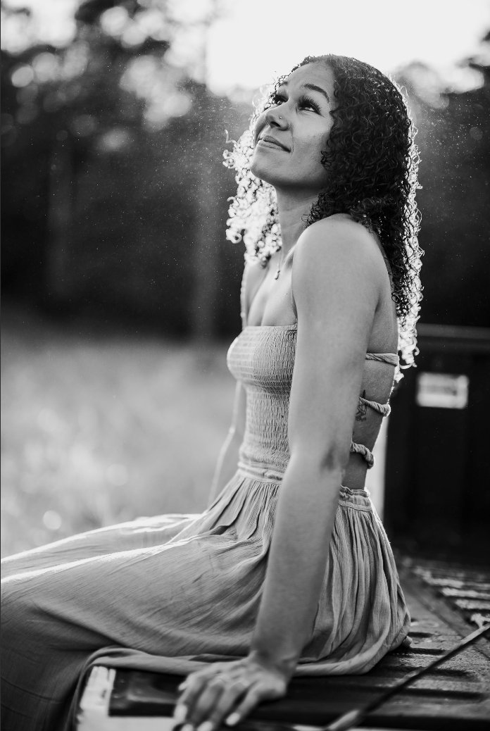 Black and white portrait of a young woman with curly hair sitting outdoors in soft bokeh lighting.