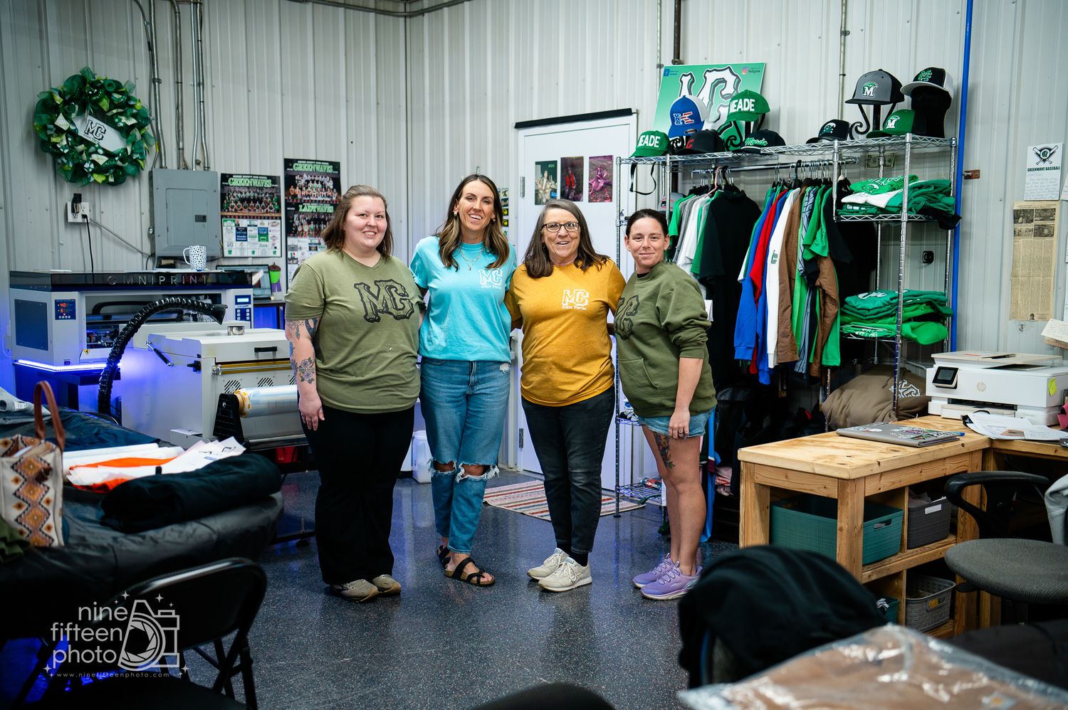 Four women smiling together inside MC Screen Printing custom apparel shop in Brandenburg Kentucky.