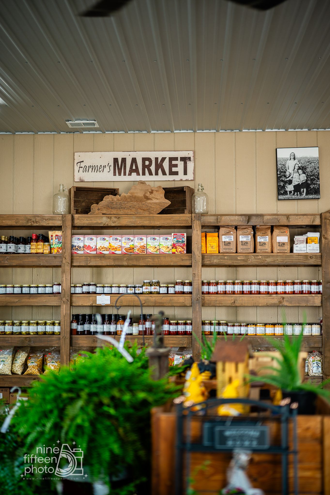 Rustic wooden shelves stocked with jars and packaged goods beneath a Farmers Market sign.