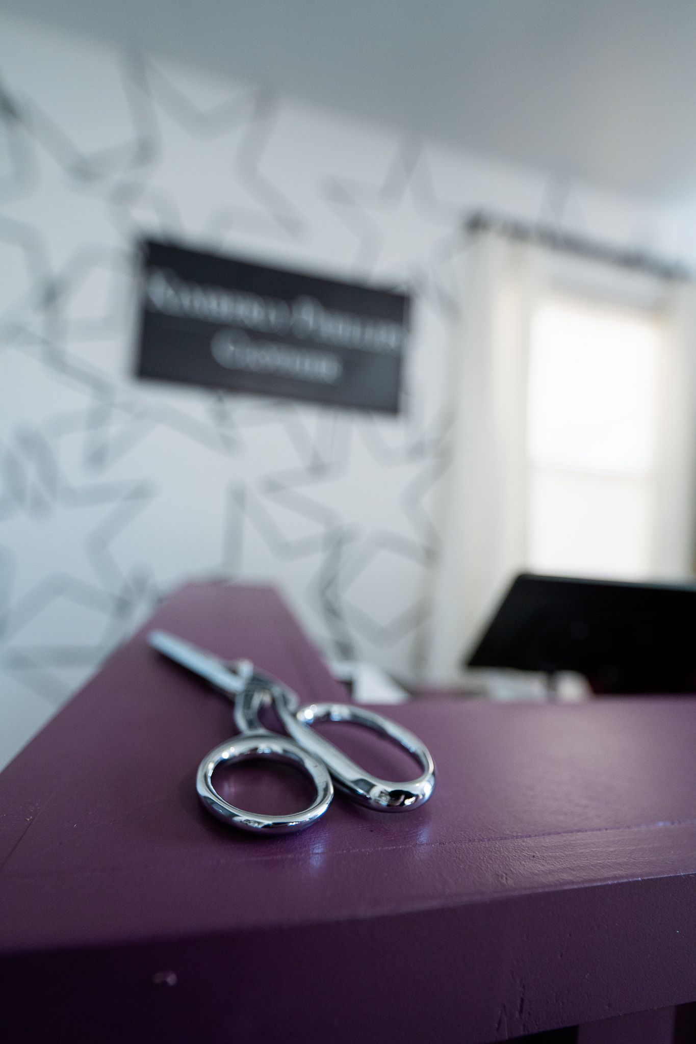 Silver scissors resting on purple surface with blurred bridal boutique sign in background.