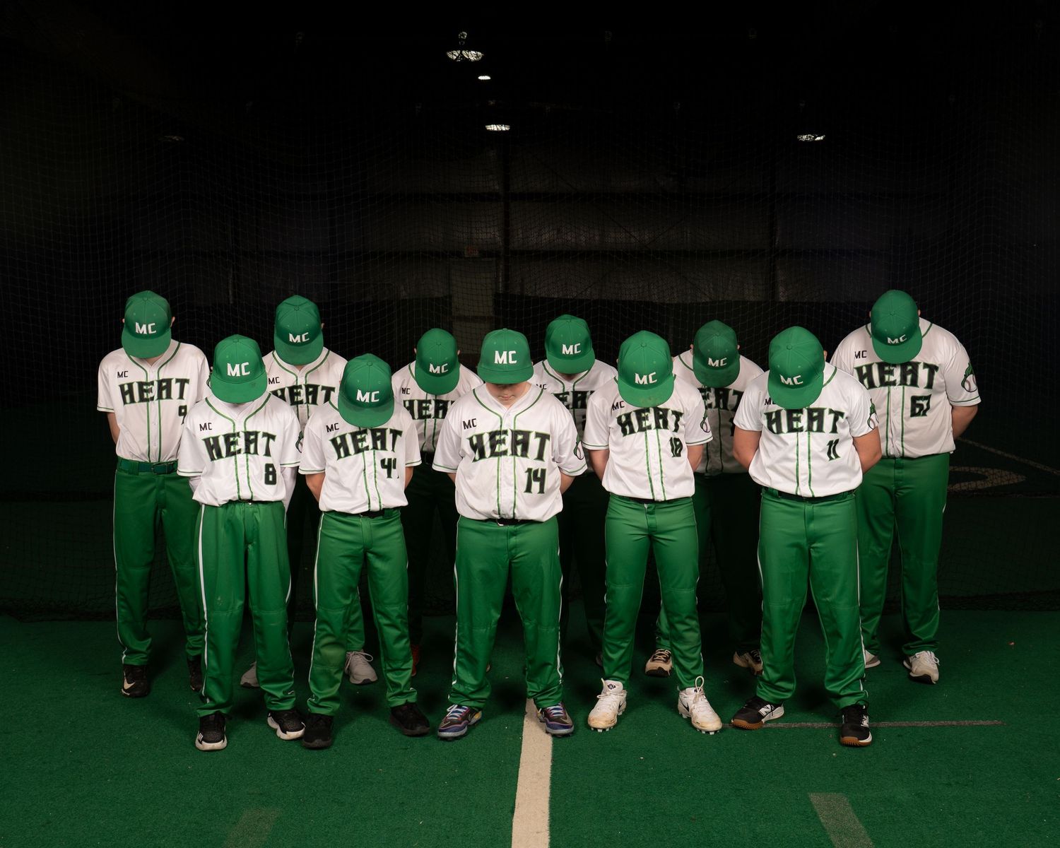 Green and white Heat baseball team posing together in uniforms with matching green caps indoors.